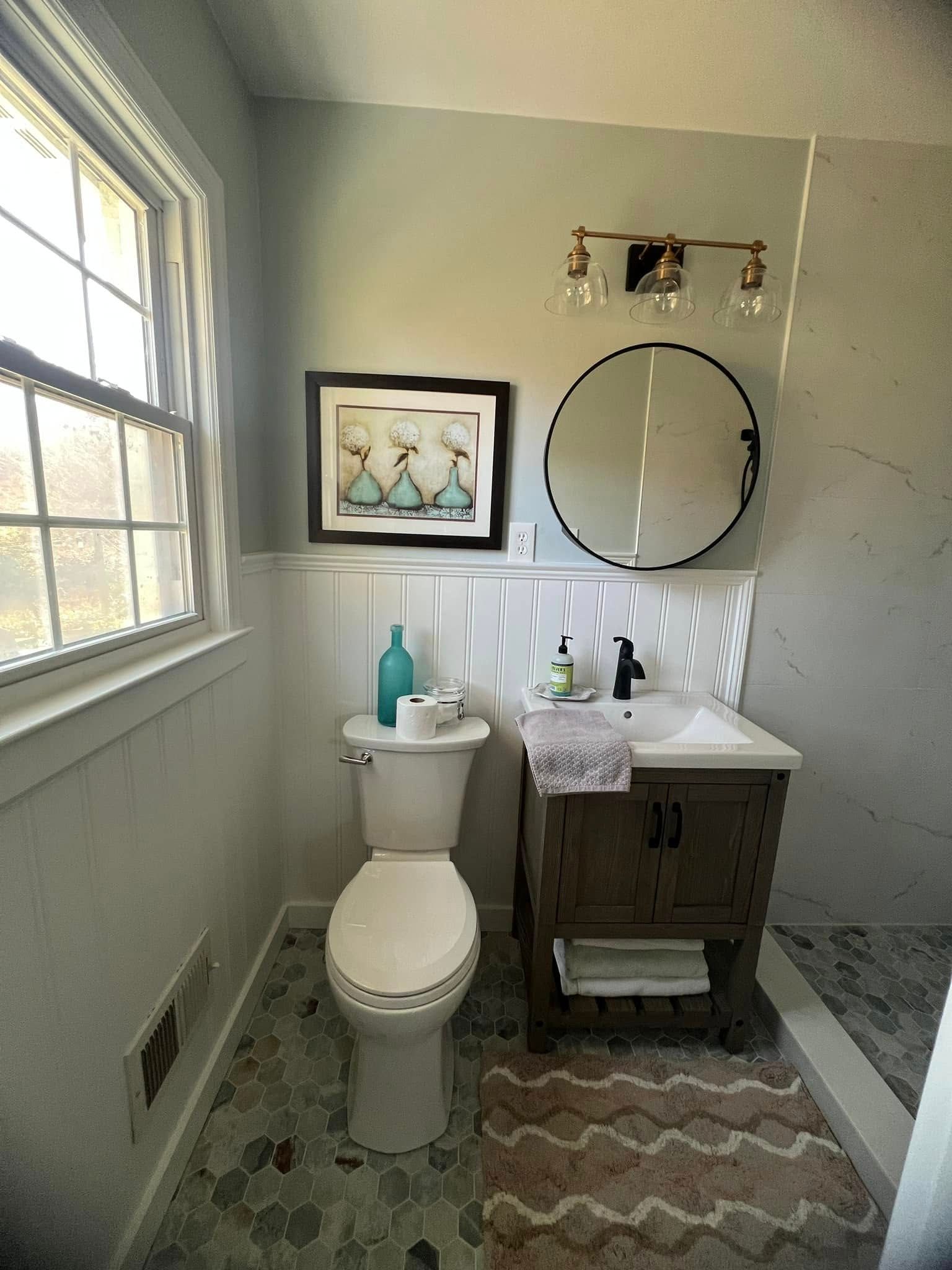 A bathroom with a toilet, sink, mirror and window.