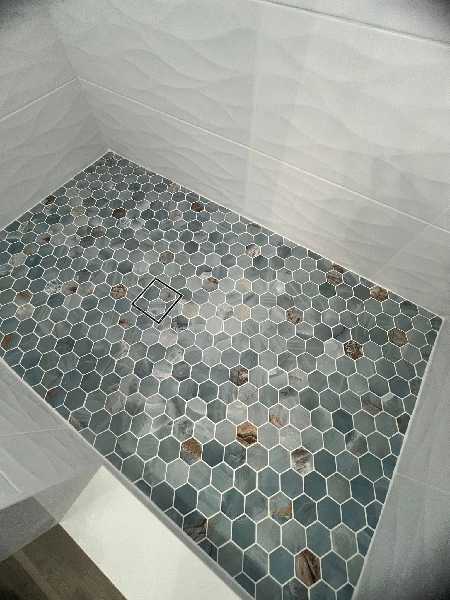 A shower stall with a hexagonal tile floor and a drain.