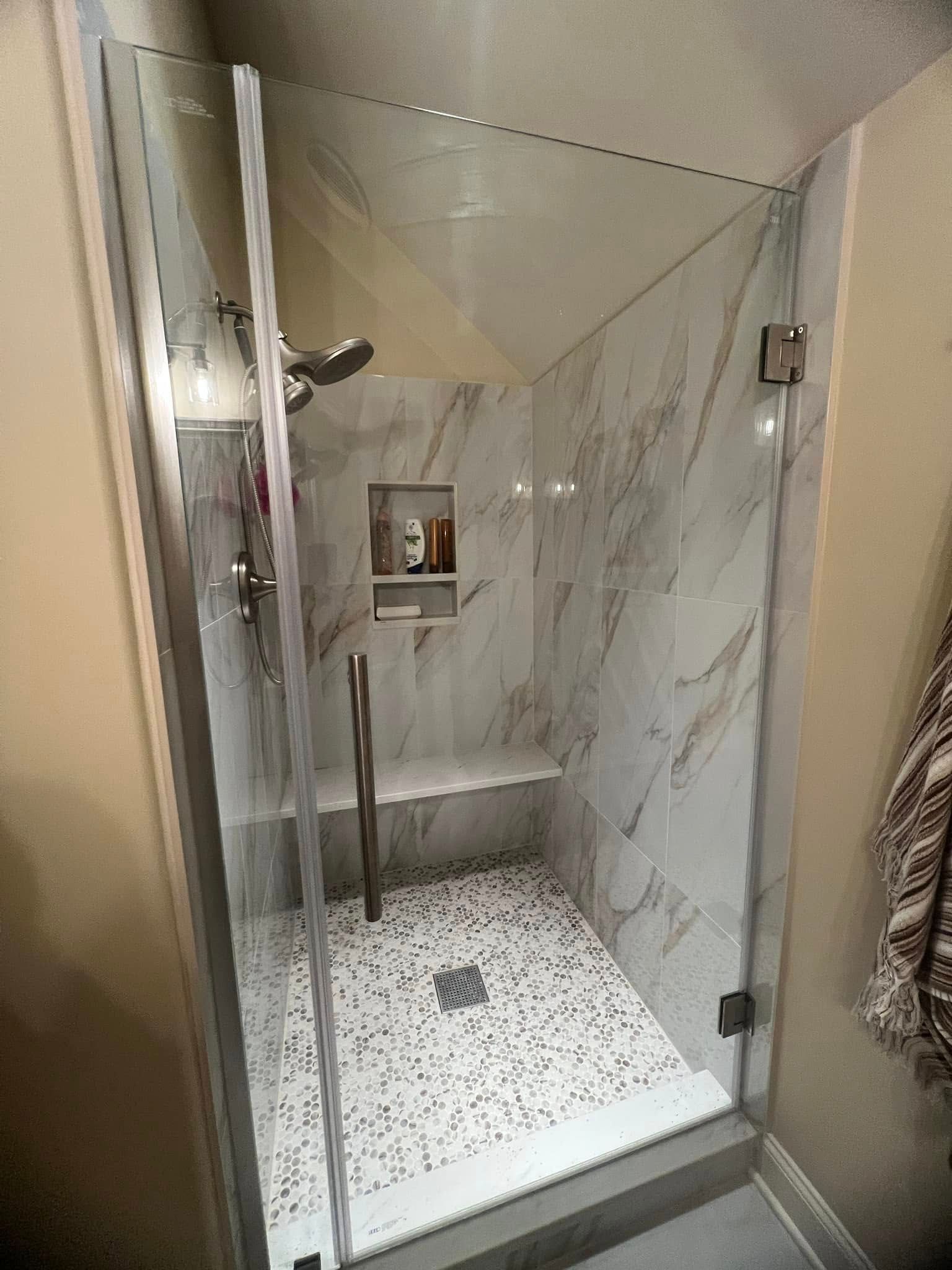 A bathroom with a walk in shower with a glass door and marble walls.