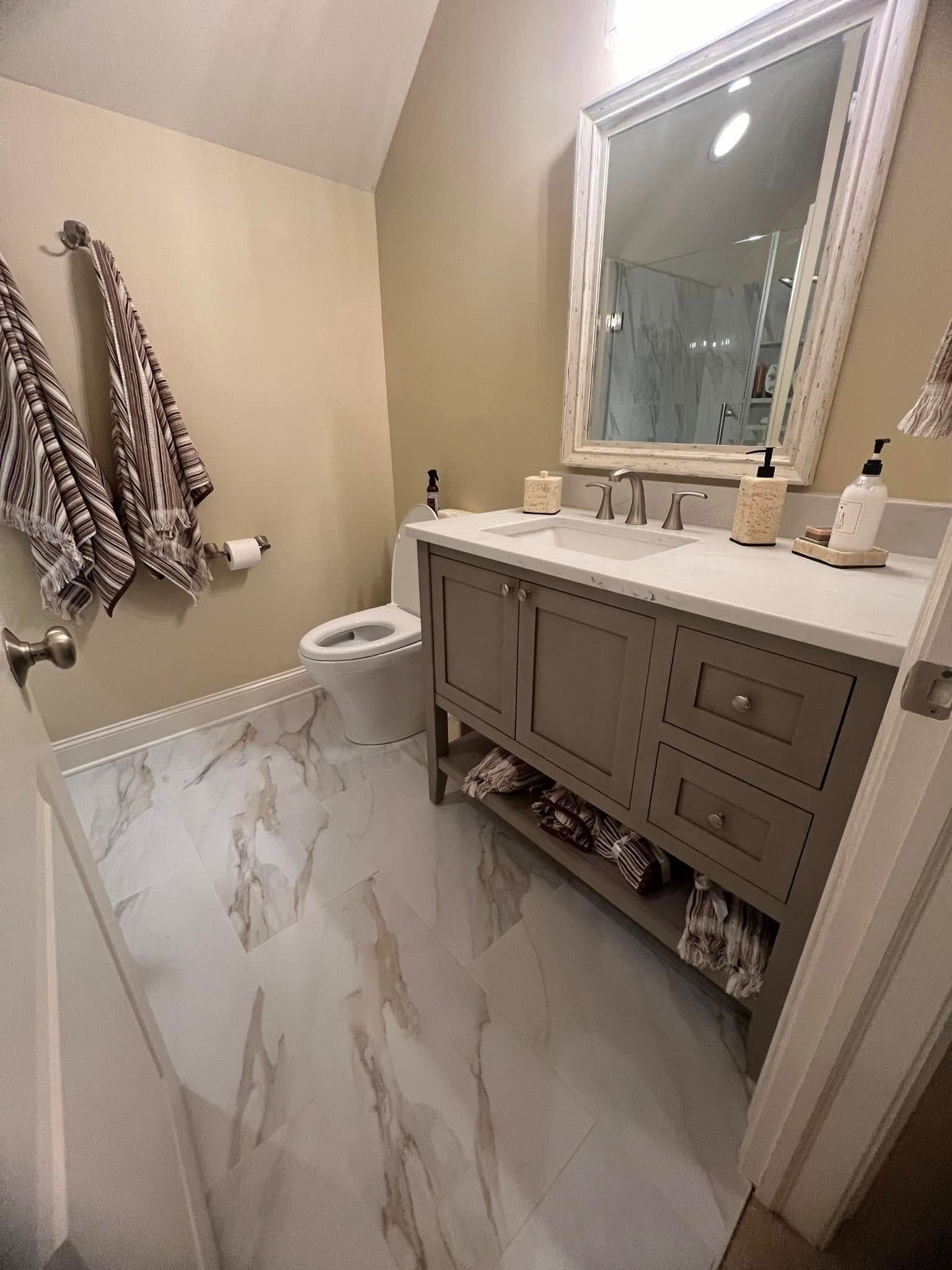A bathroom with a toilet, sink, mirror and towels hanging on the wall.