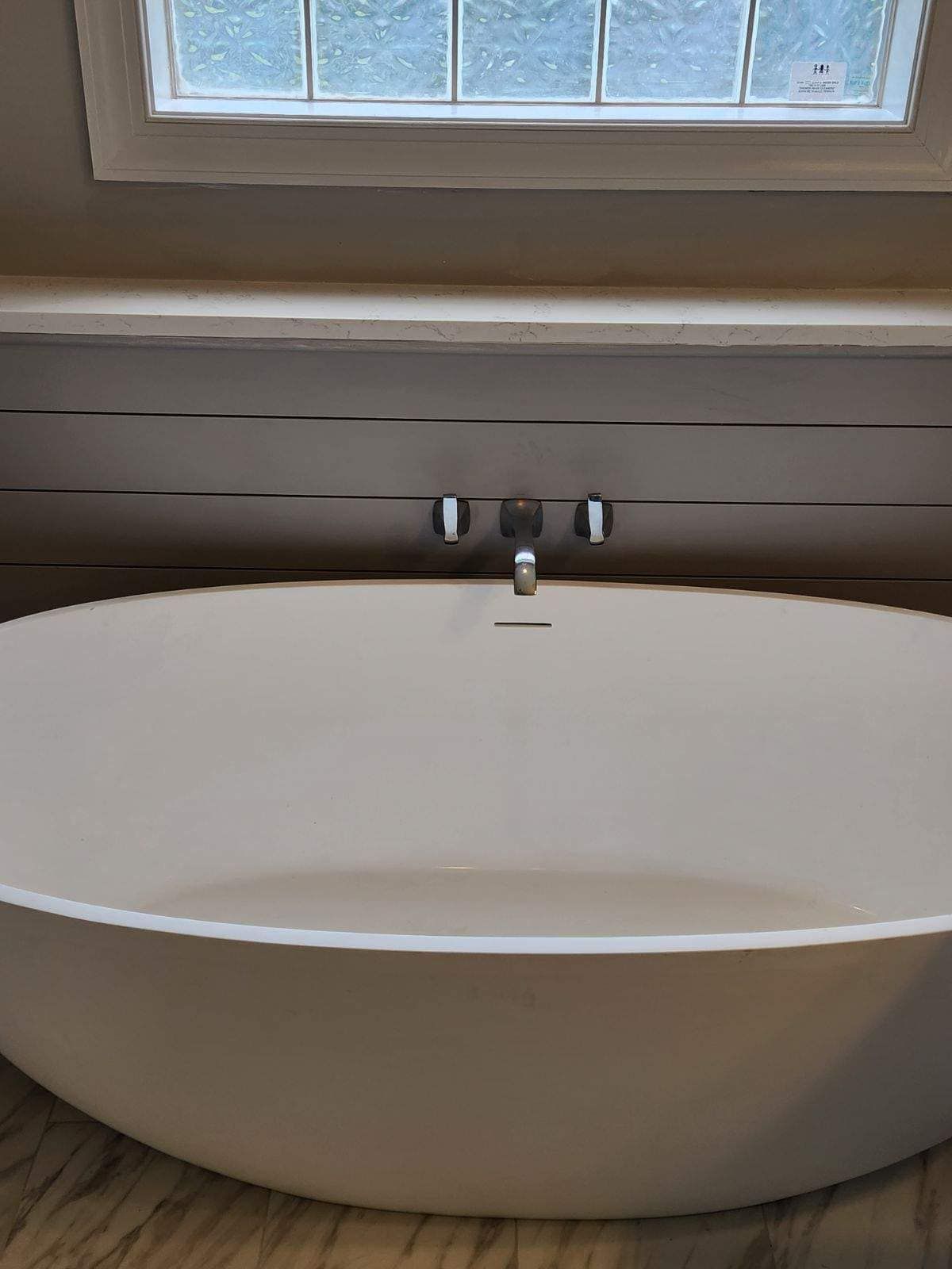A white bathtub in a bathroom next to a window