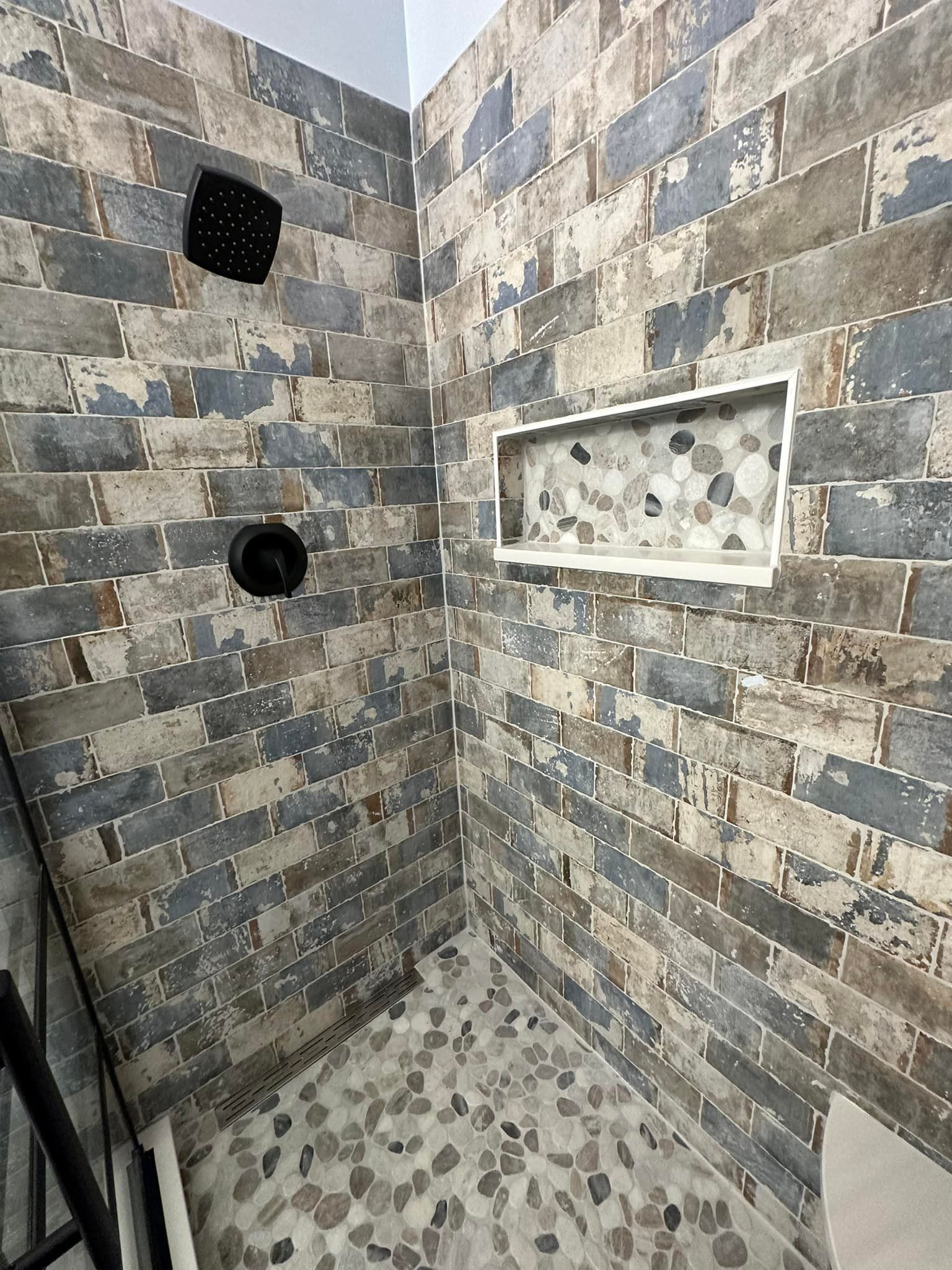 A shower with a brick wall and a tiled floor.
