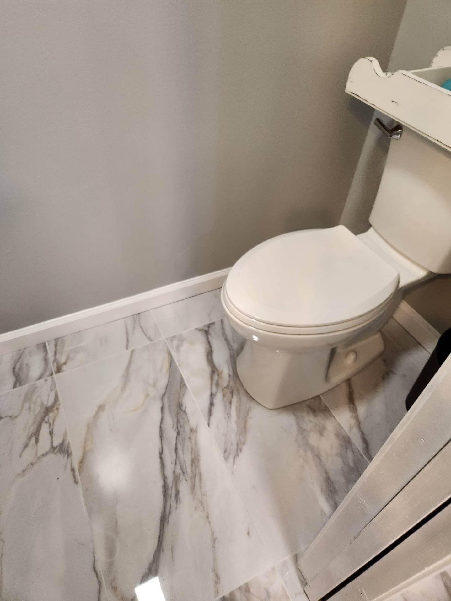 A toilet is sitting on a marble floor in a bathroom.