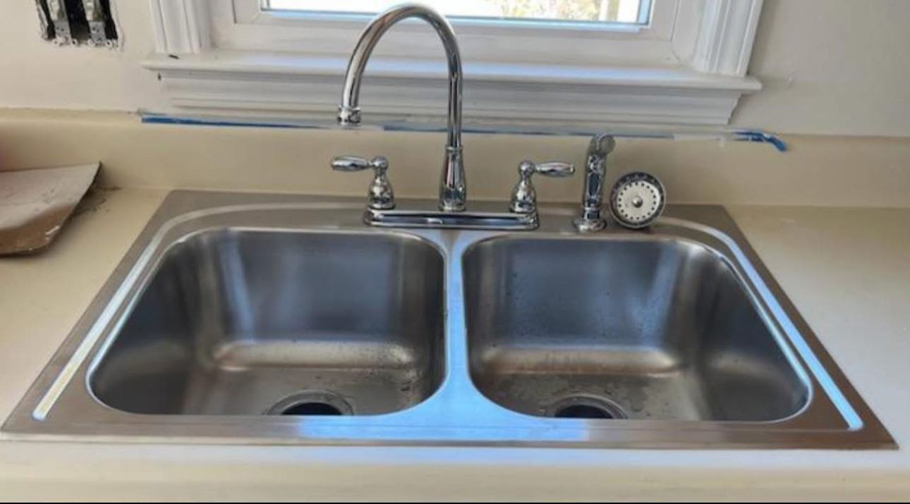 A stainless steel kitchen sink with a faucet and a clock on the counter.