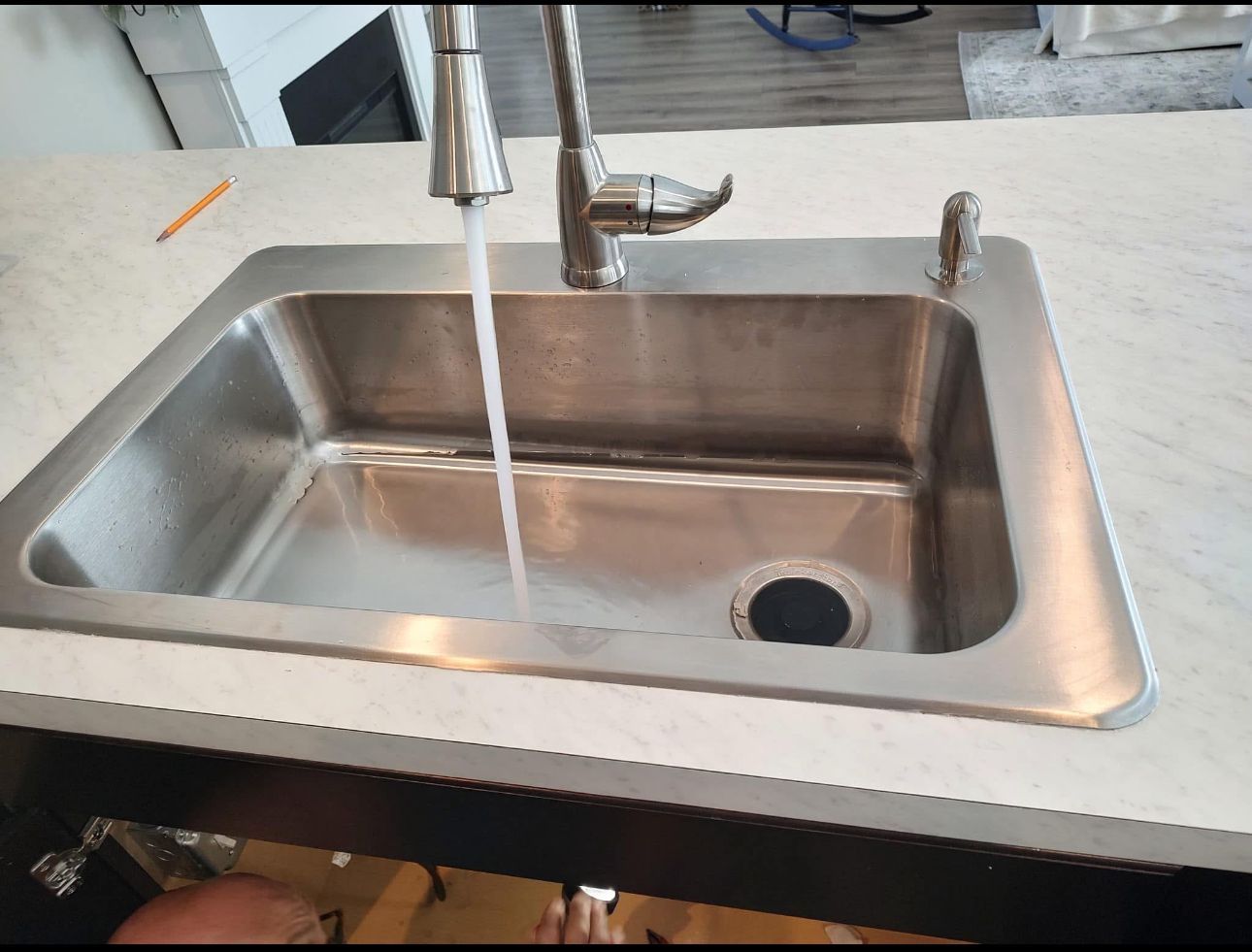 A stainless steel kitchen sink with water running from the faucet.