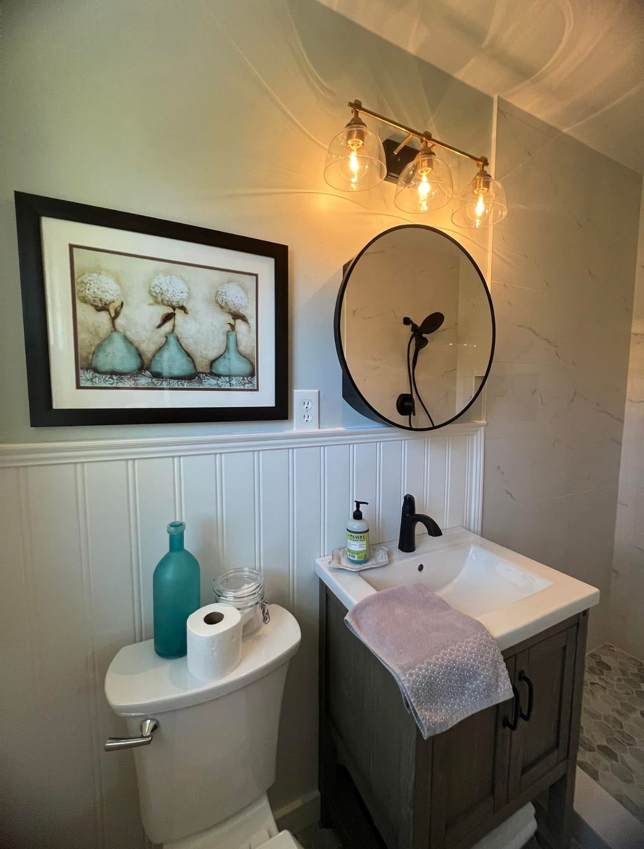 A bathroom with a toilet, sink, mirror, and picture on the wall.
