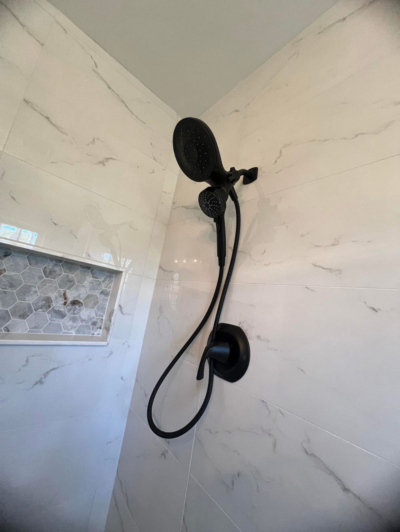 A black shower head is hanging on a white wall in a bathroom.