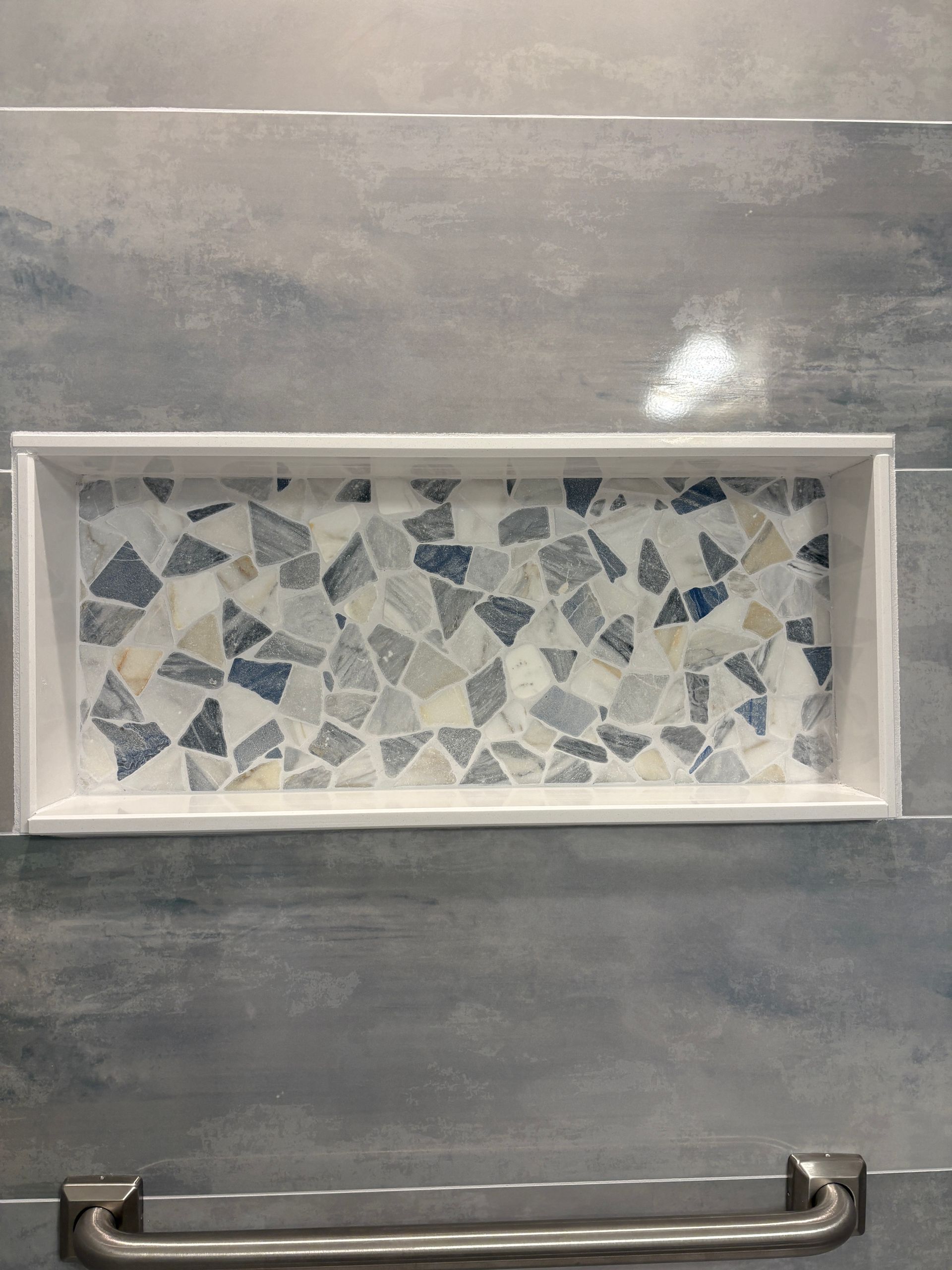 A shower niche with a mosaic tile design and a towel bar.