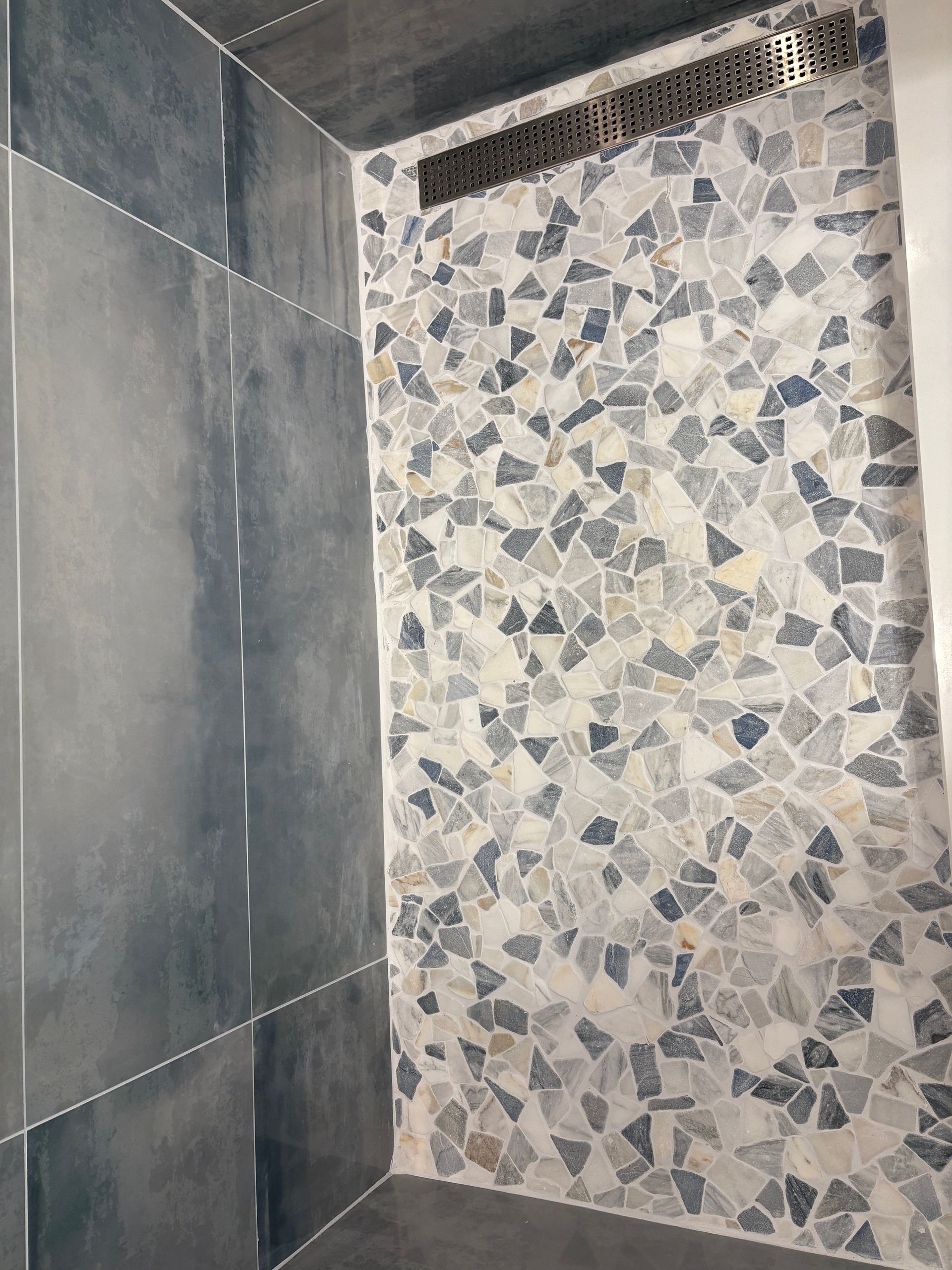 A shower stall with a tiled wall and a drain.