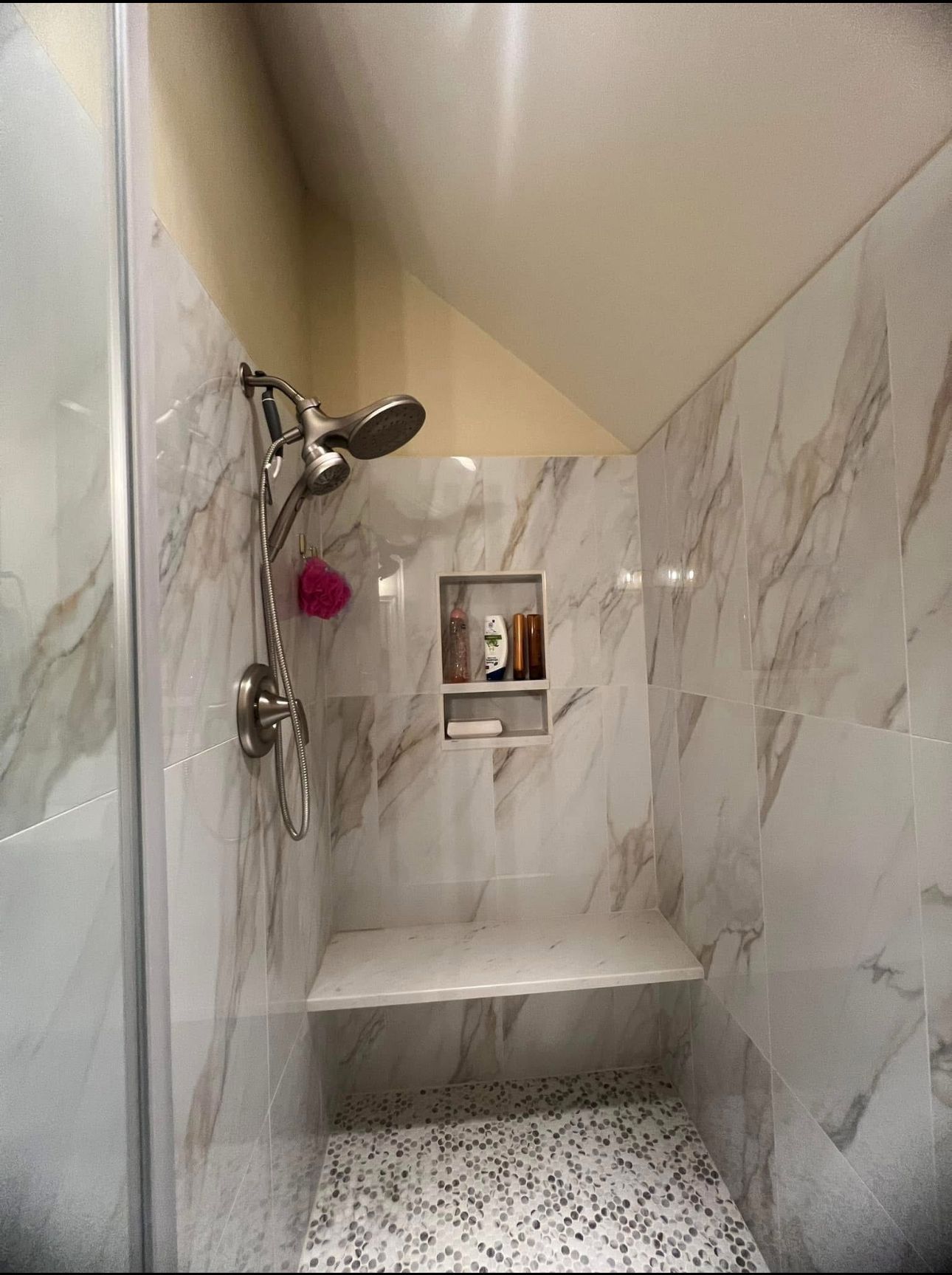 A shower with a bench and a shower head in a bathroom.