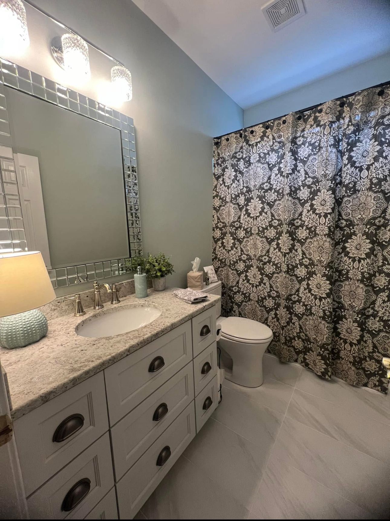 A bathroom with a sink, toilet, mirror, and shower curtain.