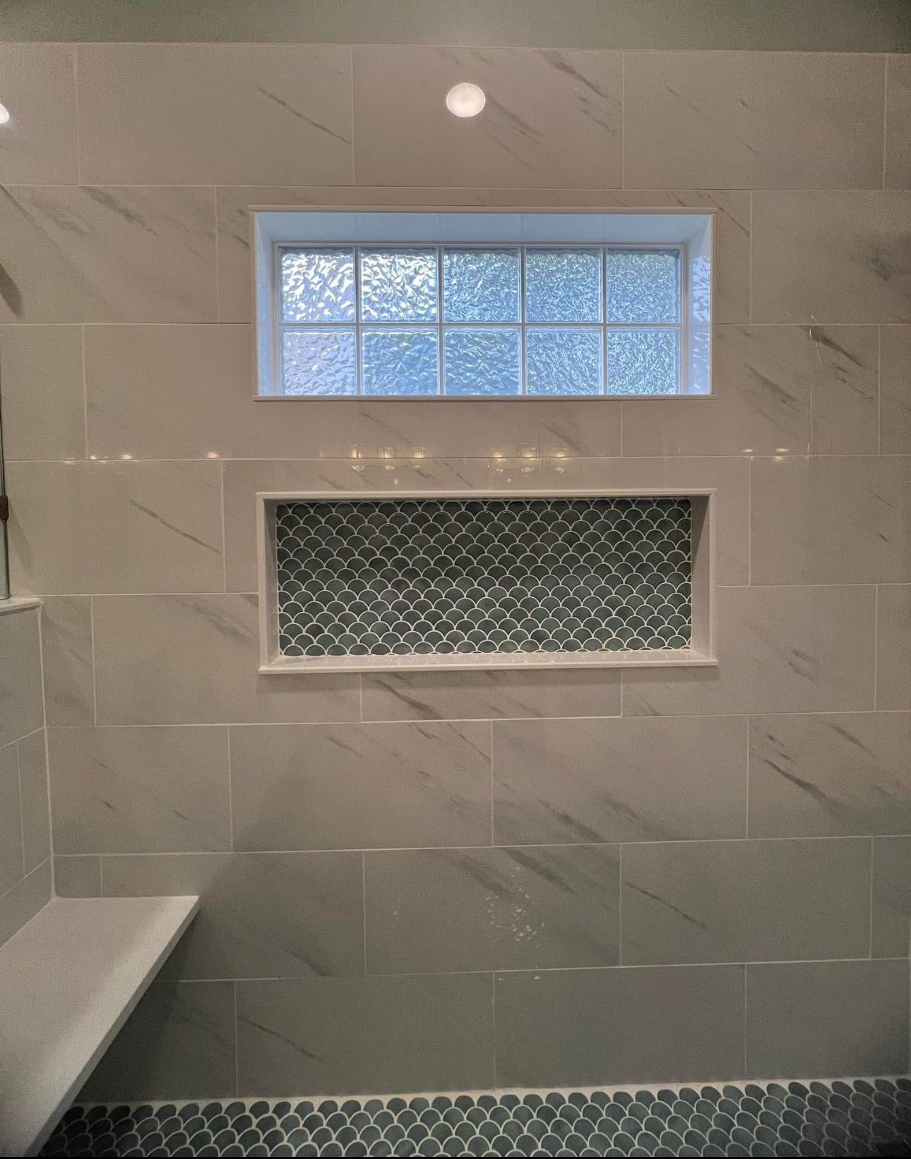A bathroom with a window and a shelf in the shower.