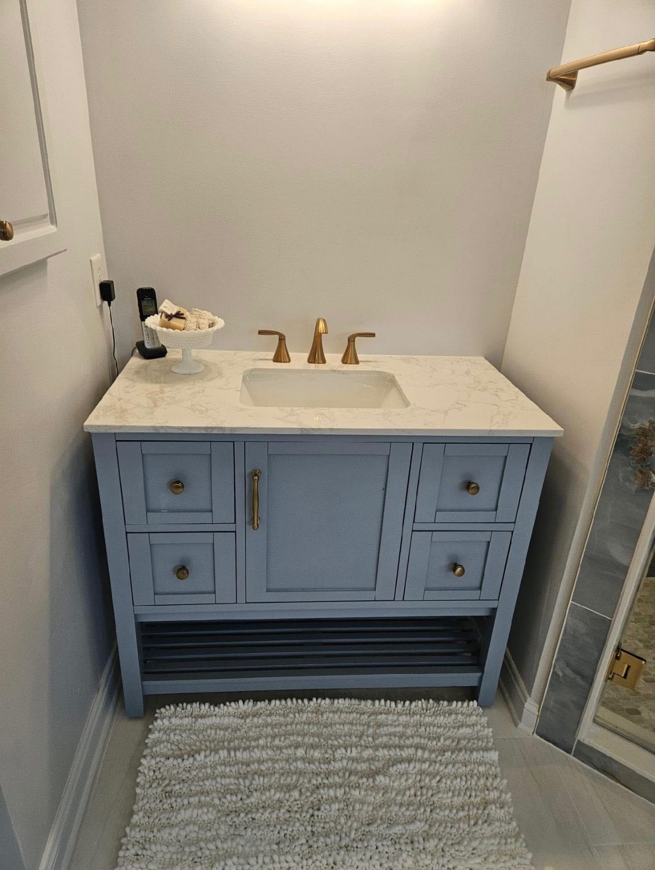 A bathroom with a blue vanity, sink, and rug.