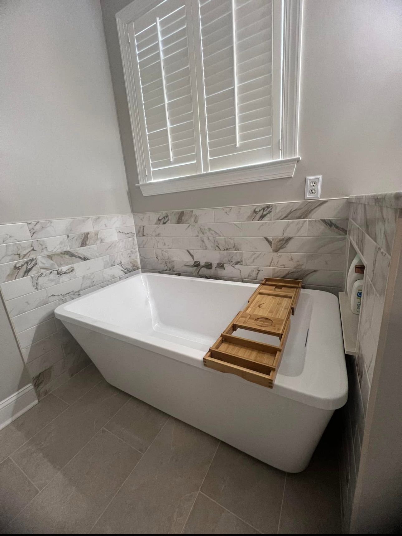 A bathroom with a bathtub and a window with shutters.