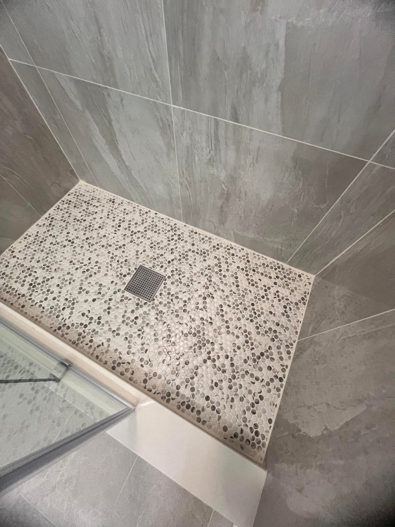 A shower stall with a tiled floor and a glass door.