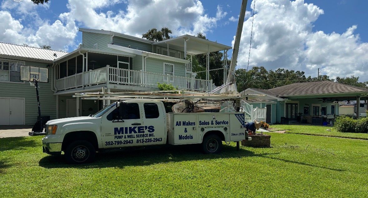 White utility truck with ladder parked on grass in front of a house under repair