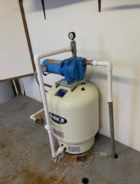 Blue pump and cream-colored tank in a utility room, connected with white pipes.