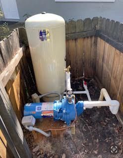 Blue water pump beside beige pressure tank in a fenced outdoor utility area