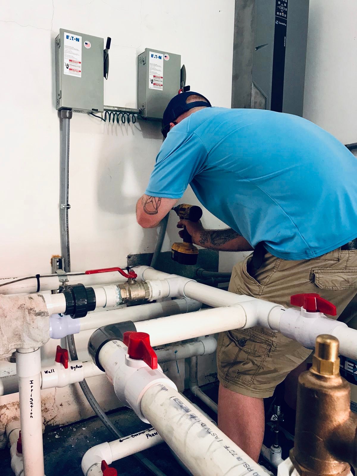 Plumber in blue shirt fixing white pipes and valves in a utility room