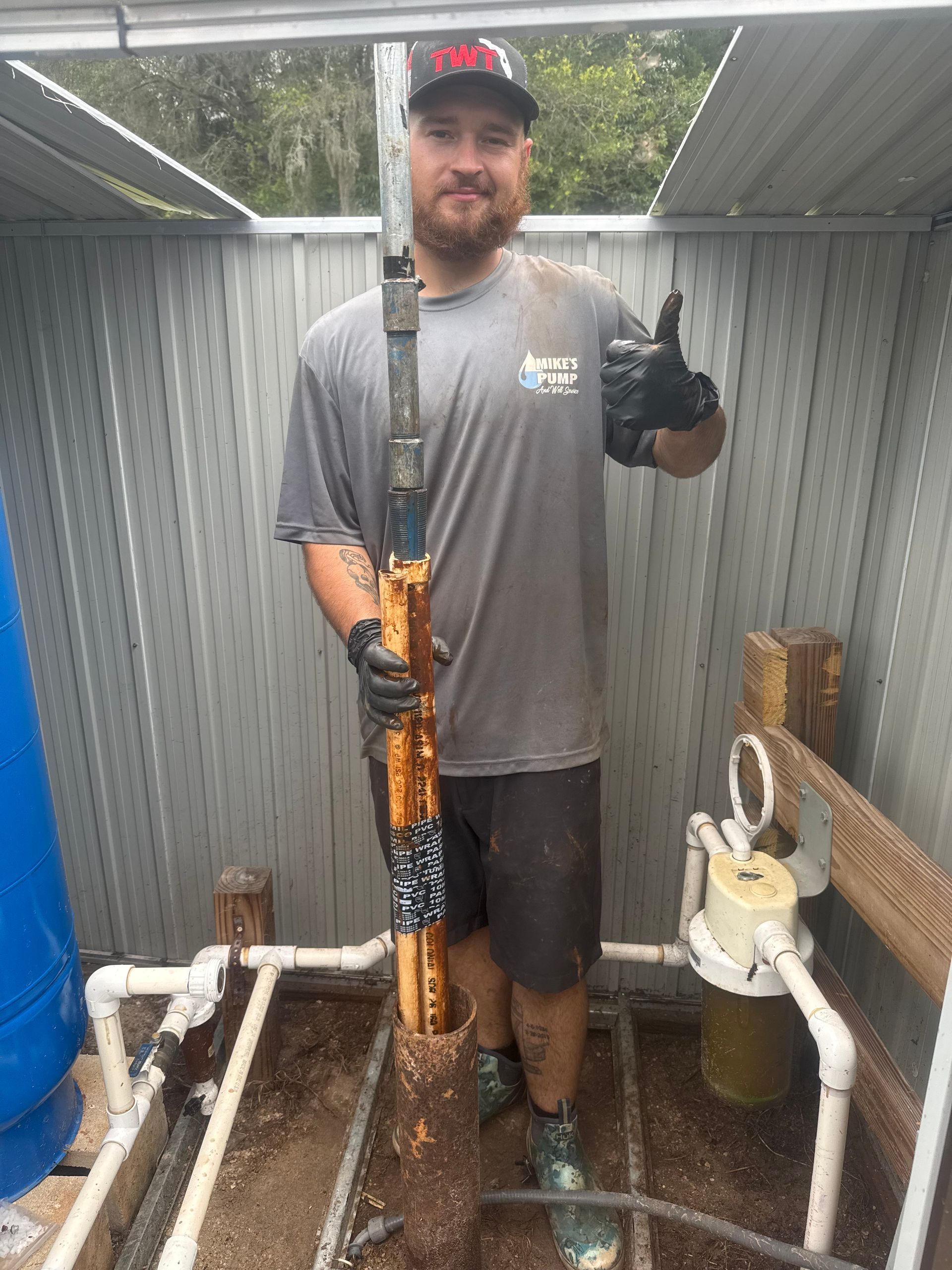 Worker standing in a utility shed holding a pressure-washing hose and giving a thumbs up