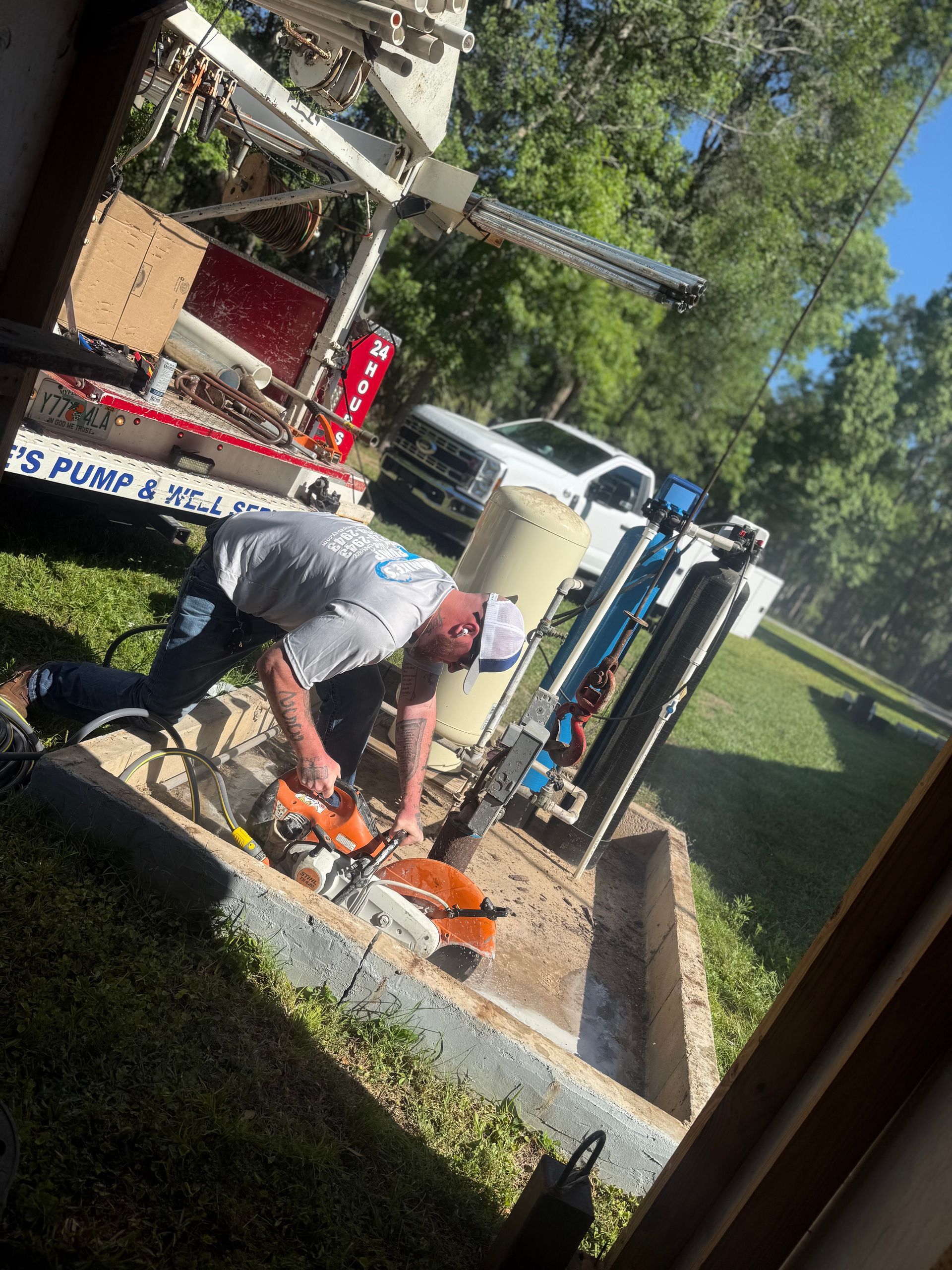 Worker in gray shirt using an orange chainsaw beside a utility truck in a grassy roadside area