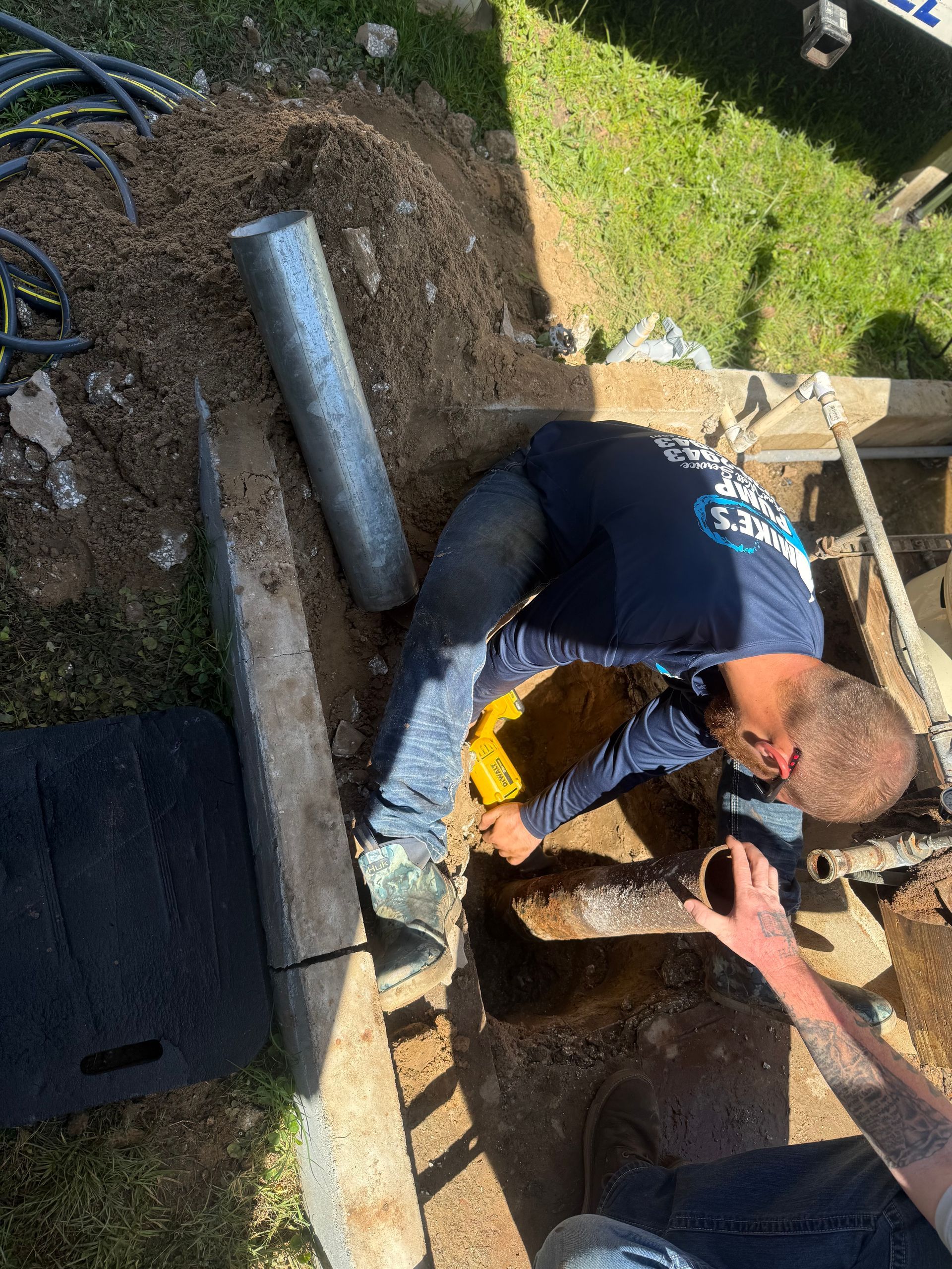 Two workers digging a trench beside a house, moving soil with shovels and a yellow tool.