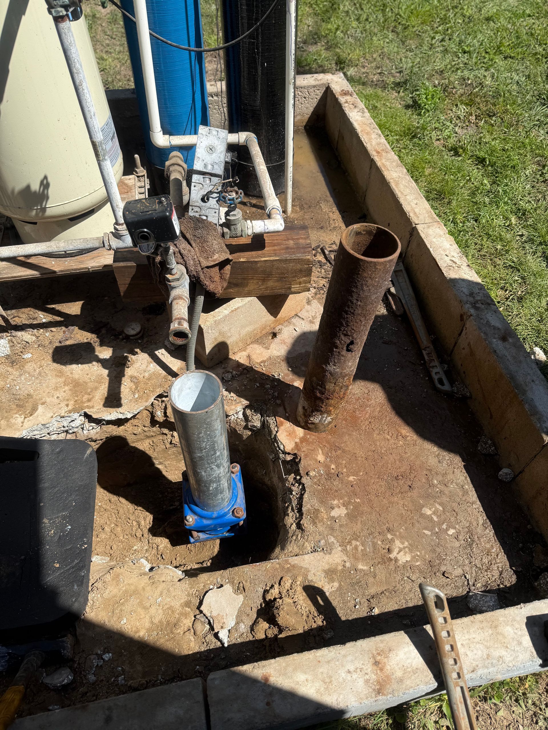 Drilling equipment over a concrete pad with exposed metal pipes and dirt around the base