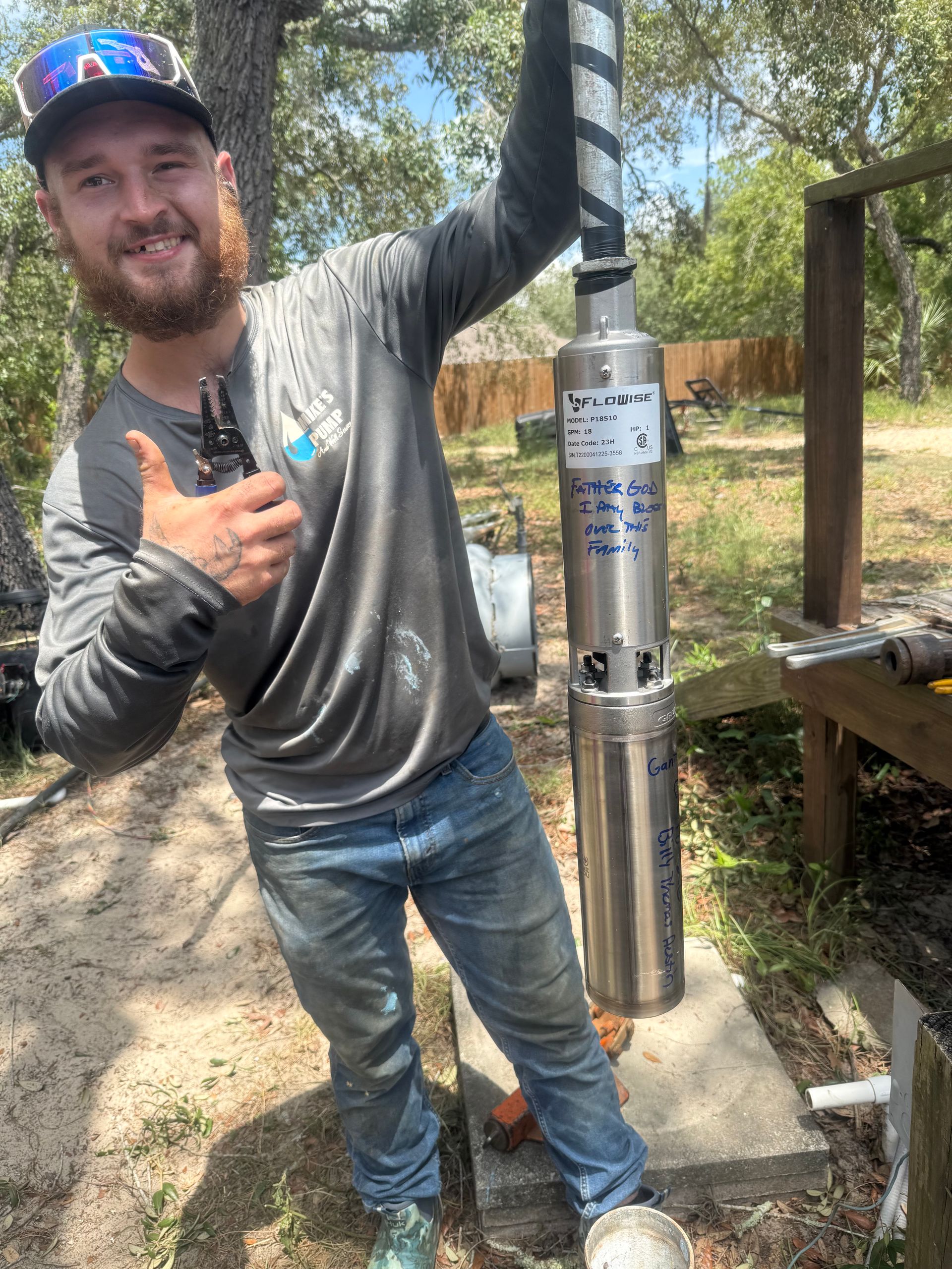 Man posing beside a metal post in a wooded outdoor area, giving a thumbs-up and smiling.