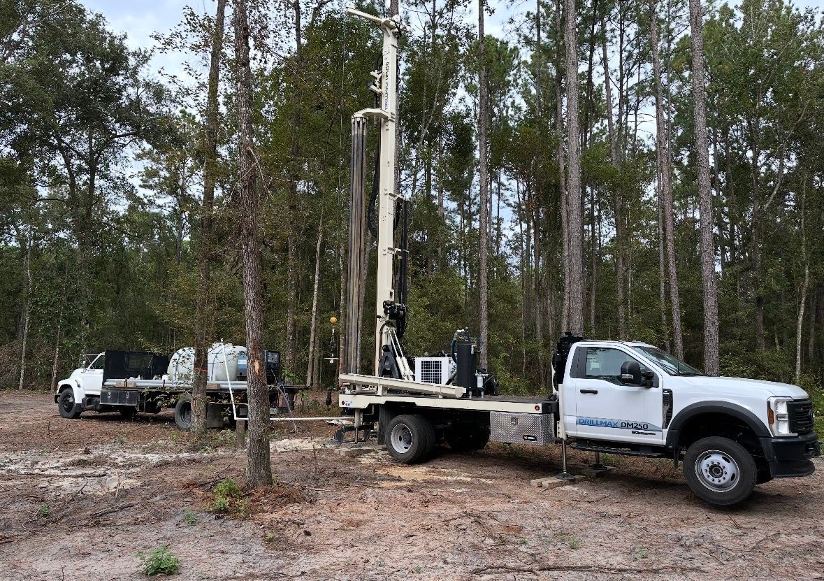 White utility truck with equipment parked in a wooded area, with another truck in the background.