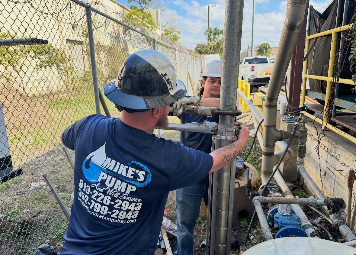 Worker in hard hat adjusting industrial piping beside a pump at an outdoor utility site