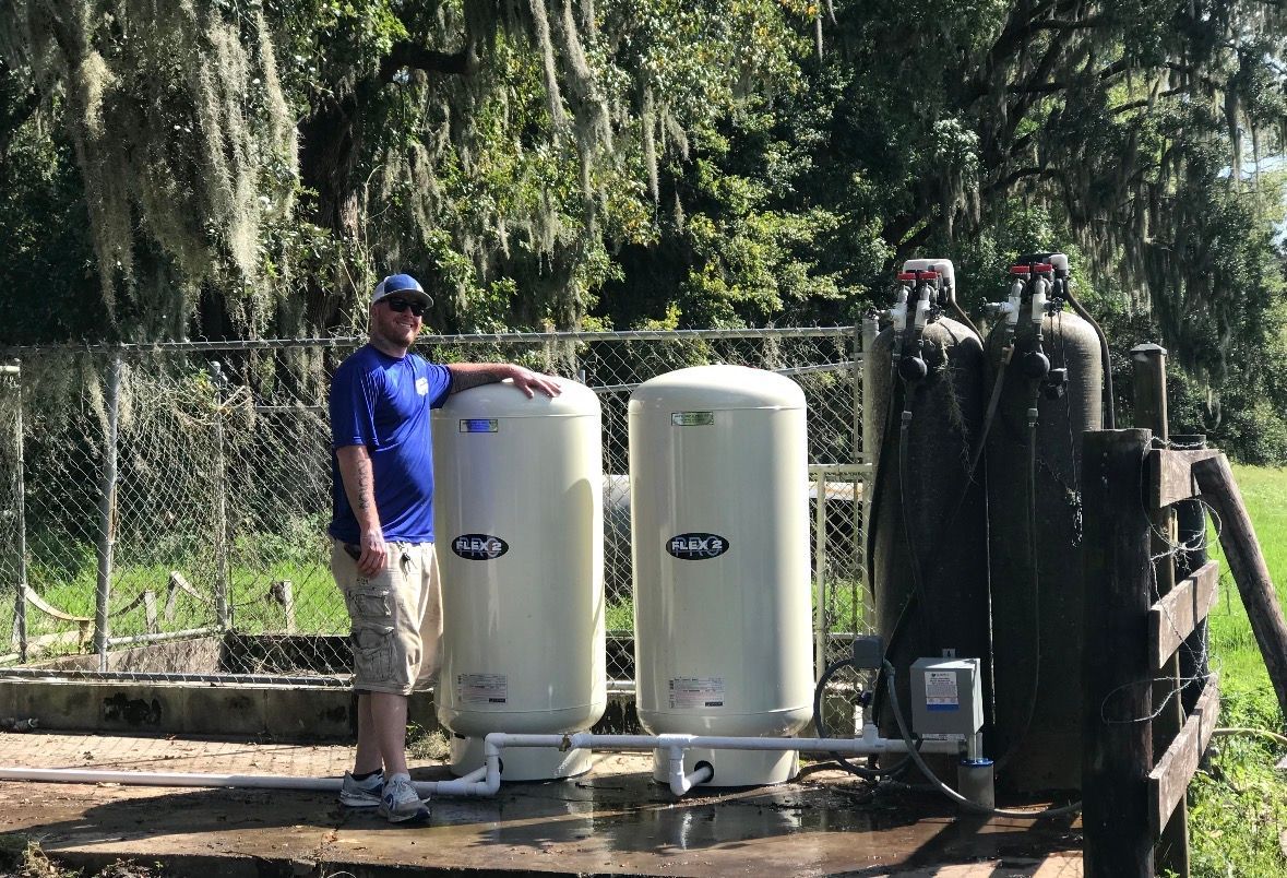 Worker beside water treatment tanks outdoors under trees