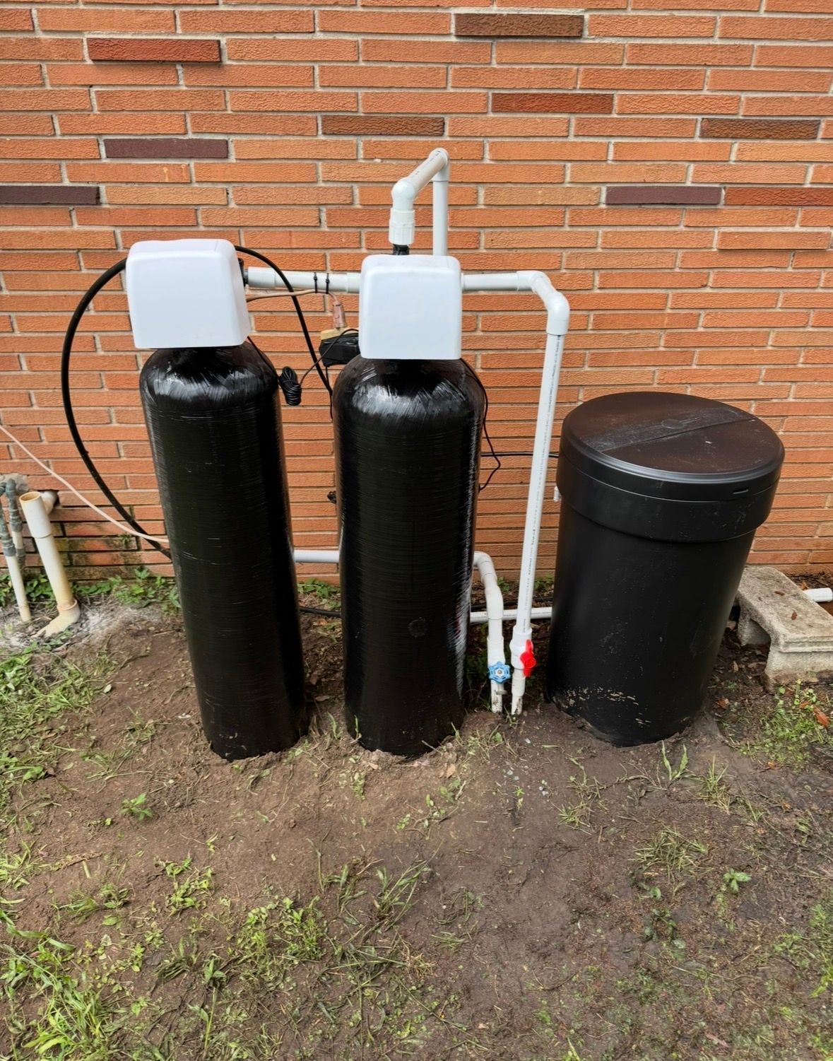 Two black water treatment tanks with white tops beside a brick wall and black cylindrical tank