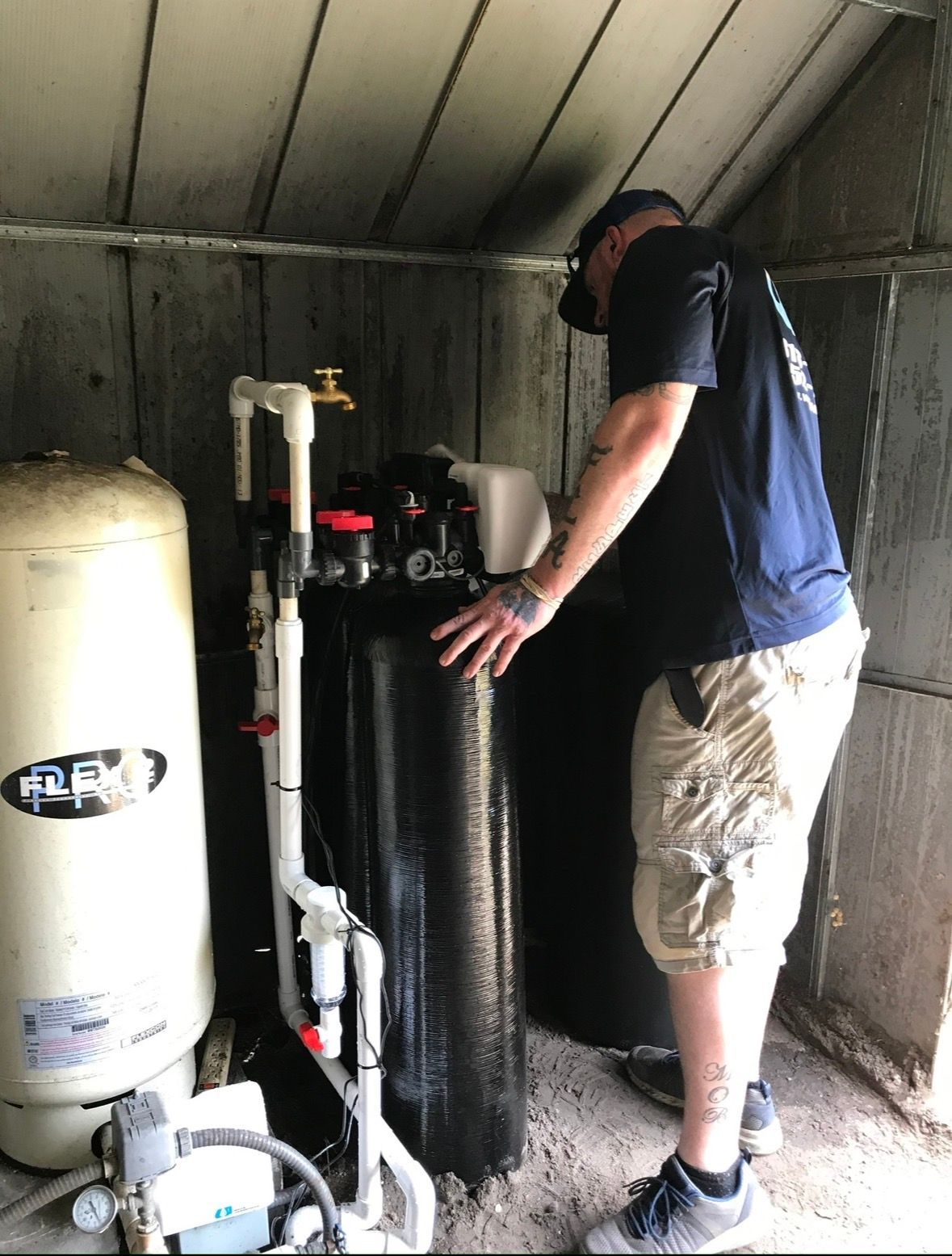 Person inspecting water filtration equipment in a small utility shed.