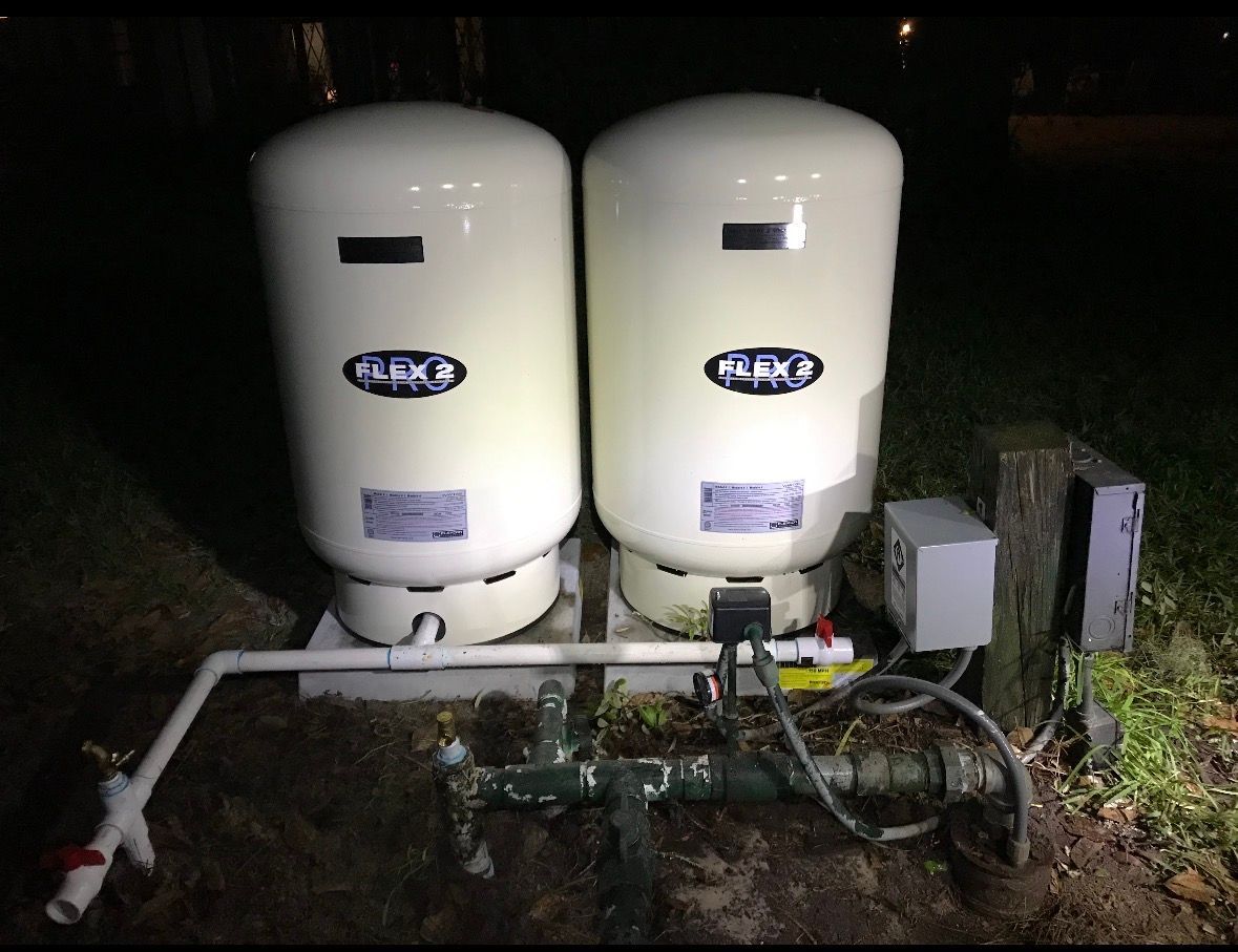 Two white outdoor pressure tanks and connected piping at night on a grassy area