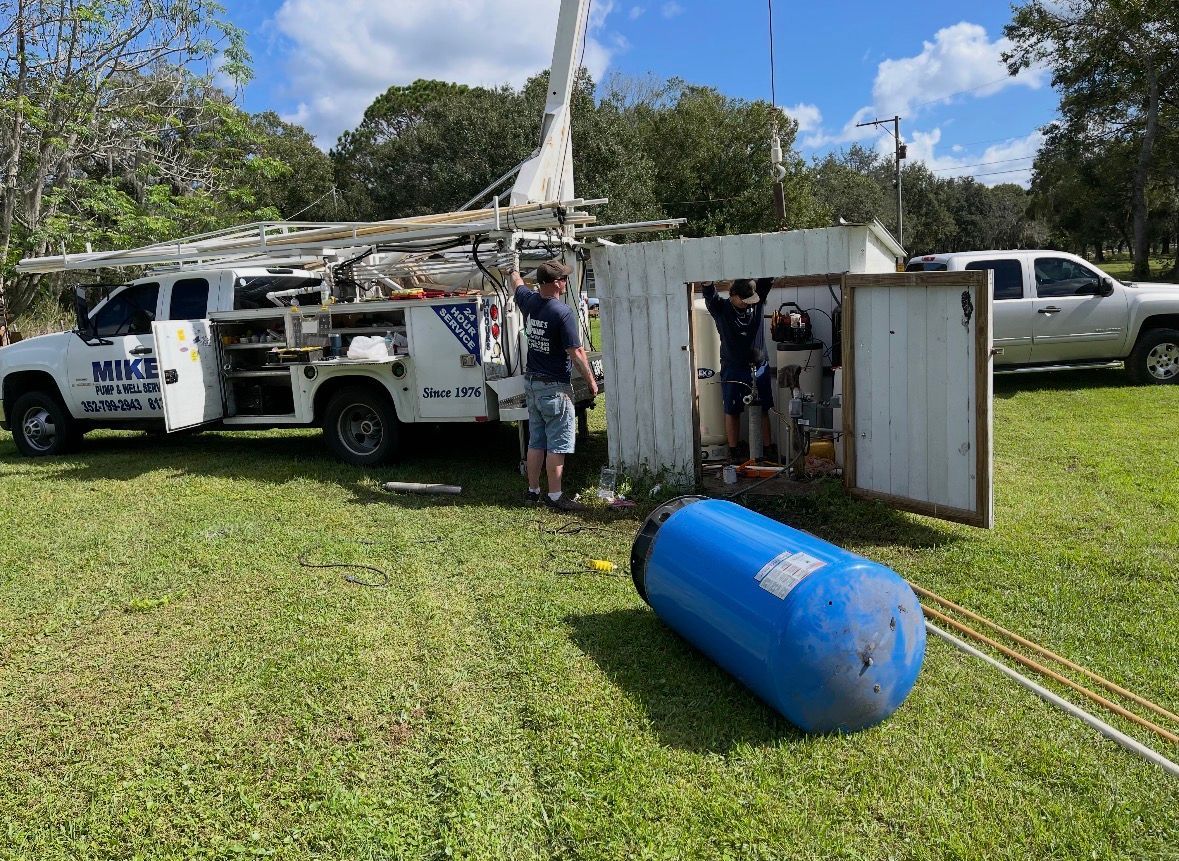 Utility truck and worker beside an overturned metal container and blue tank on a grassy field.