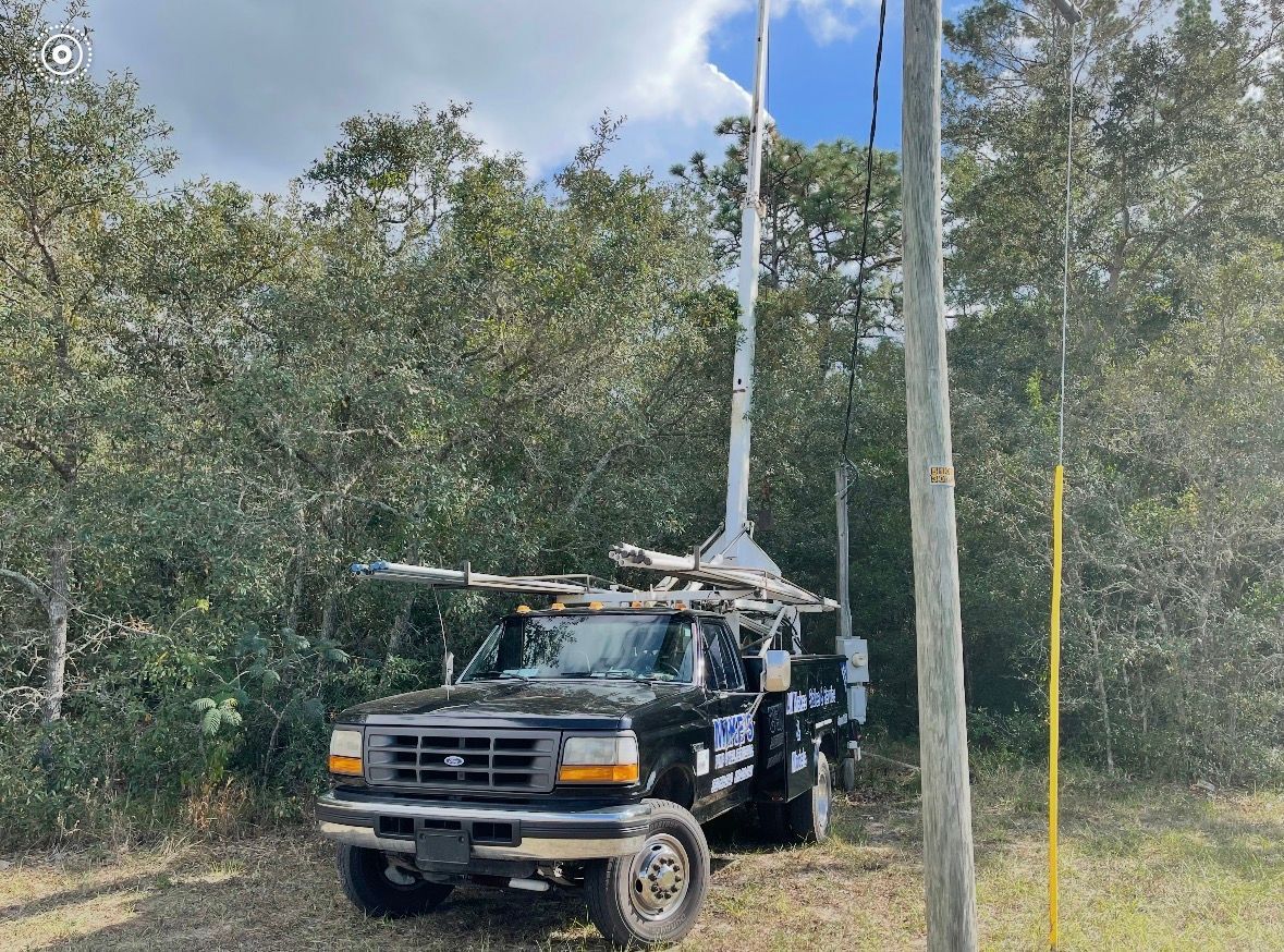 Utility truck with equipment parked under tall trees in a wooded area
