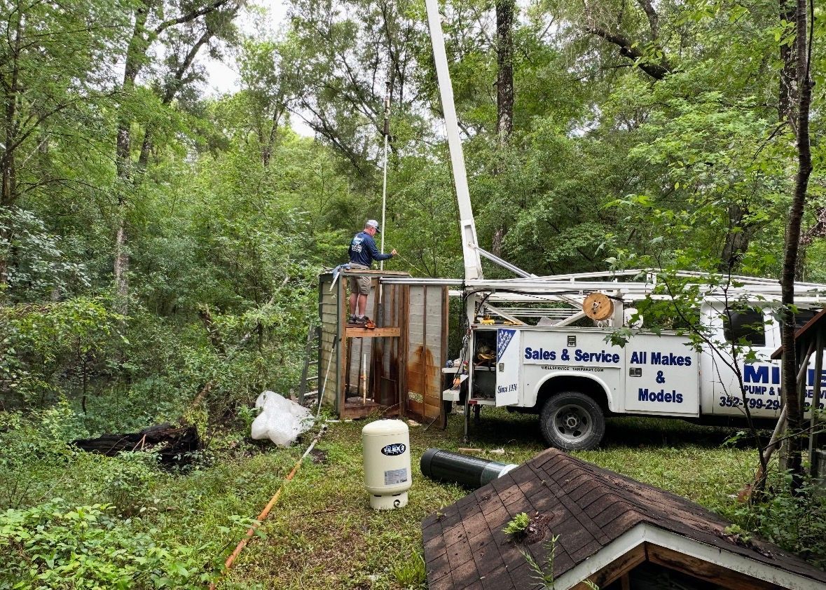 Utility truck and worker beside storm-damaged trees in a wooded yard
