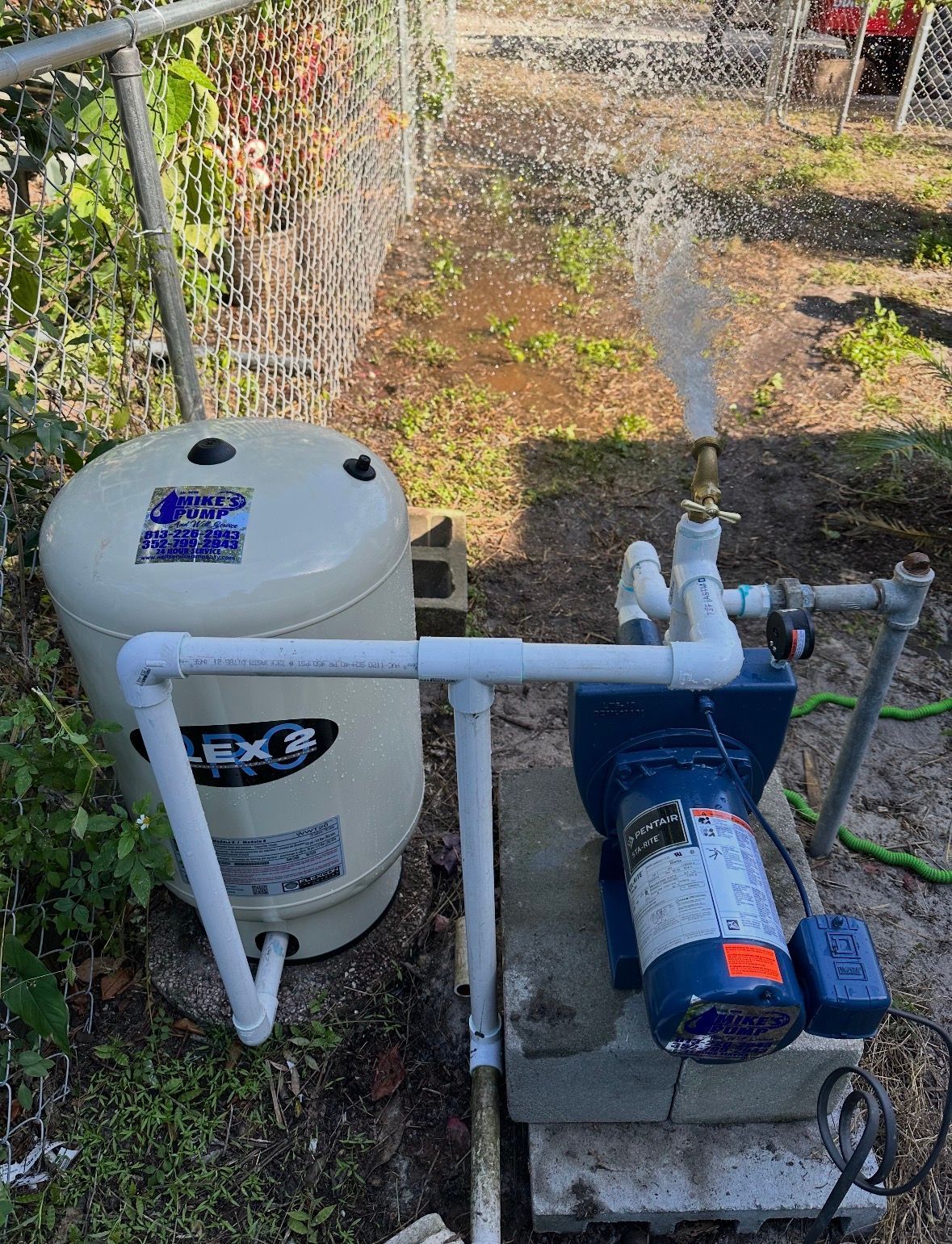 Outdoor pool filter and pump with water spraying from a sprinkler in a yard.