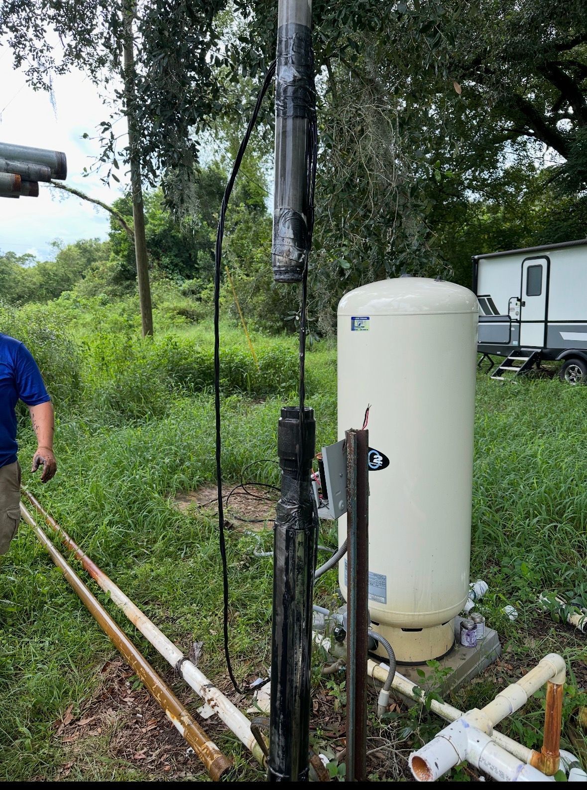 White water tank and pipes in a grassy yard, with a person partly visible at left.