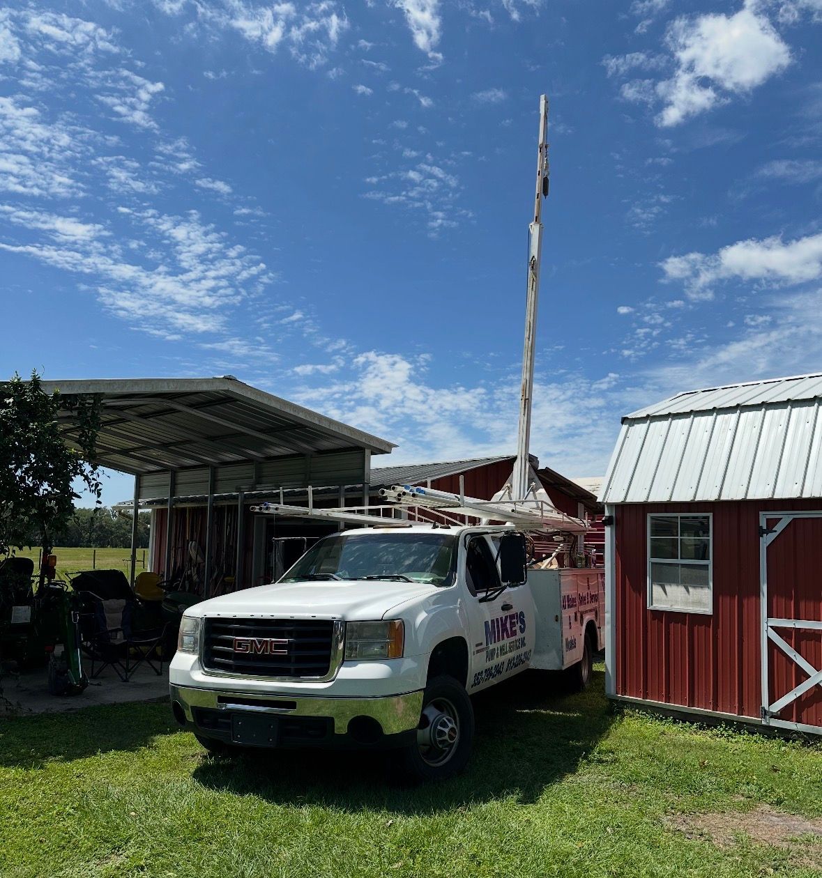 White pickup truck beside a red barn and shed on a sunny farm with grassy ground and blue sky