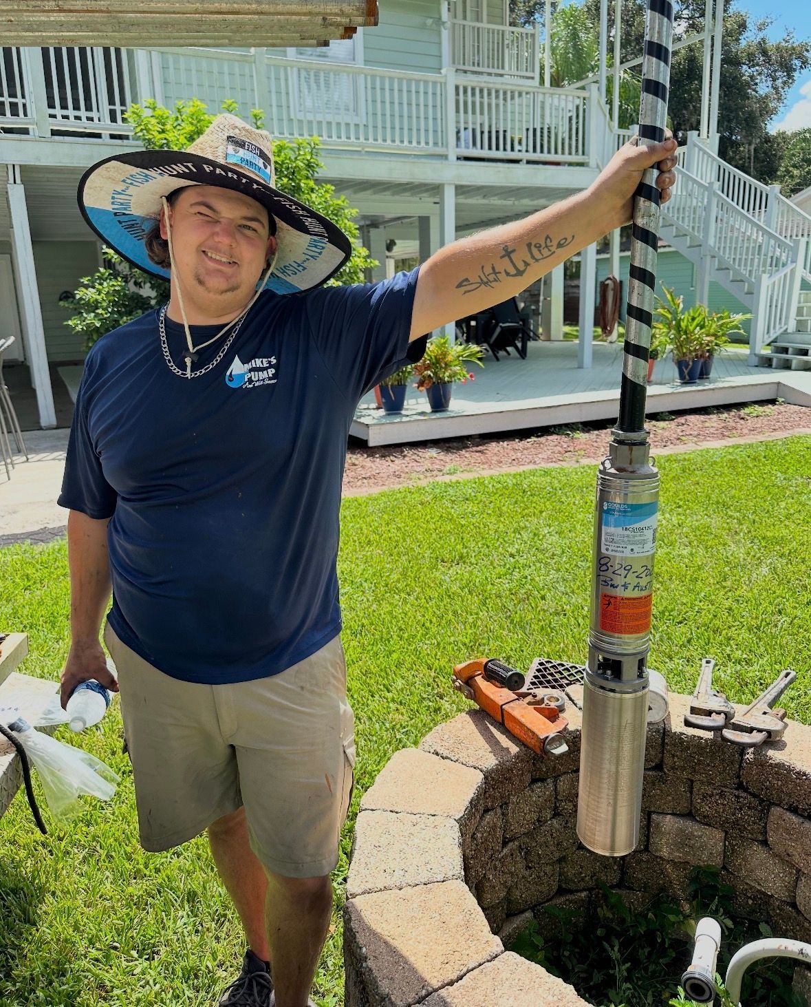 Man in a sun hat holds a tall pole beside a landscaped yard and house