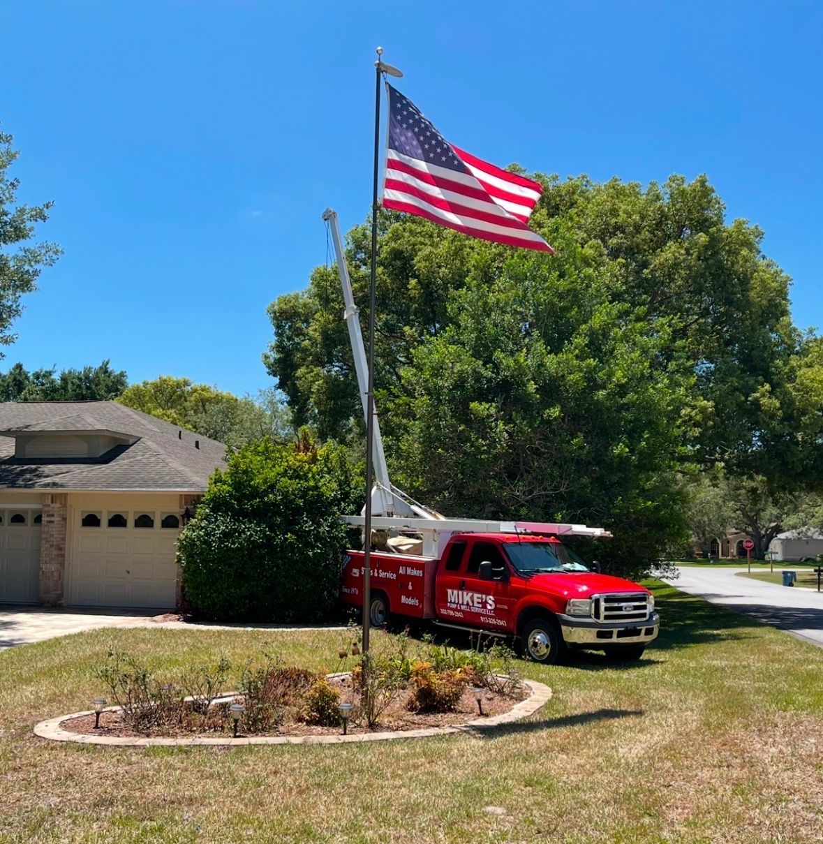 Red emergency truck parked by a driveway with a large American flag in a sunny suburban yard