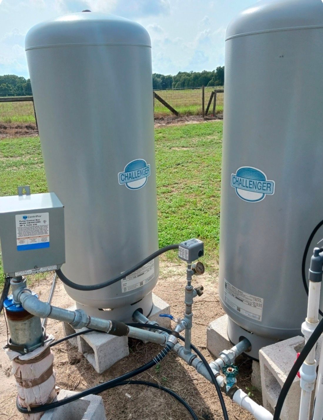 Two silver industrial tanks and pipes on concrete pads in a grassy field