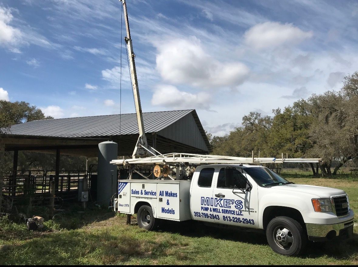 White utility truck with equipment mounted on top parked beside a building under a cloudy sky.