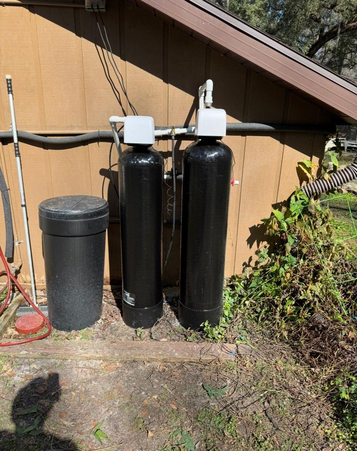 Three black water softener tanks beside a tan house, with a matching black brine tank nearby.