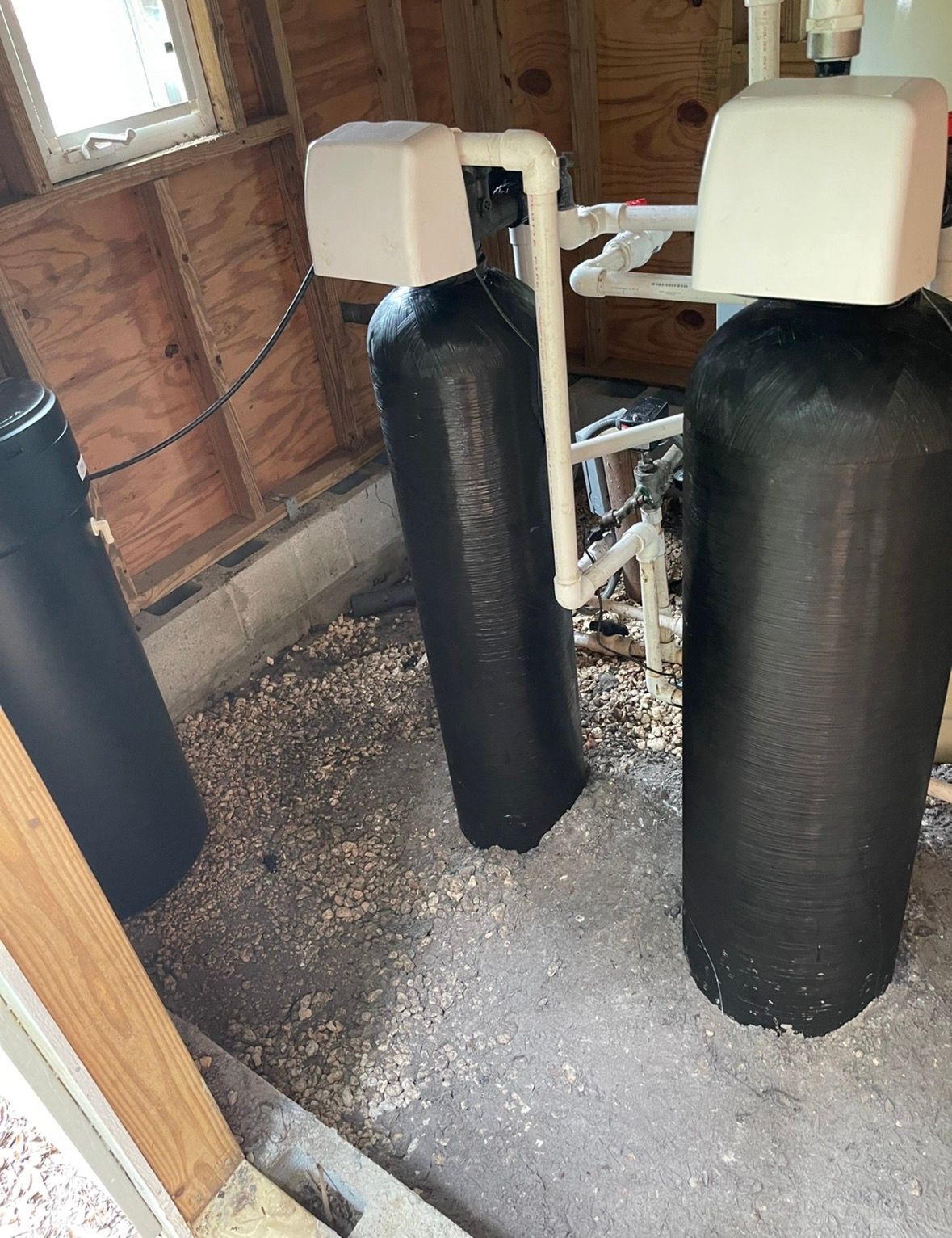 Black heavy bags with white tops in a basement workout area on a gravel floor
