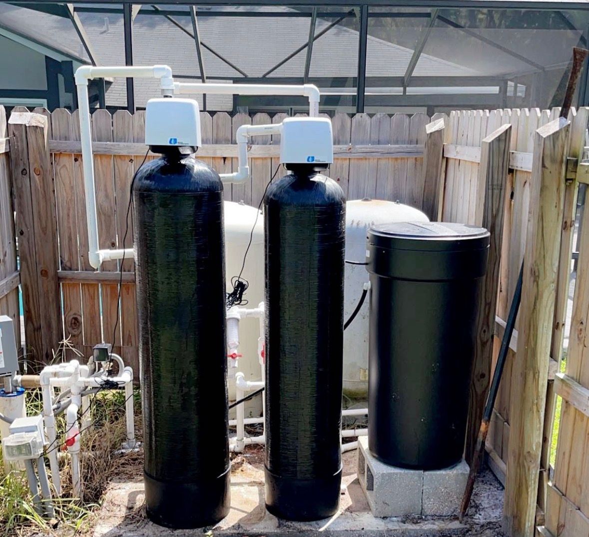 Three large black water-treatment tanks in a fenced outdoor utility area.