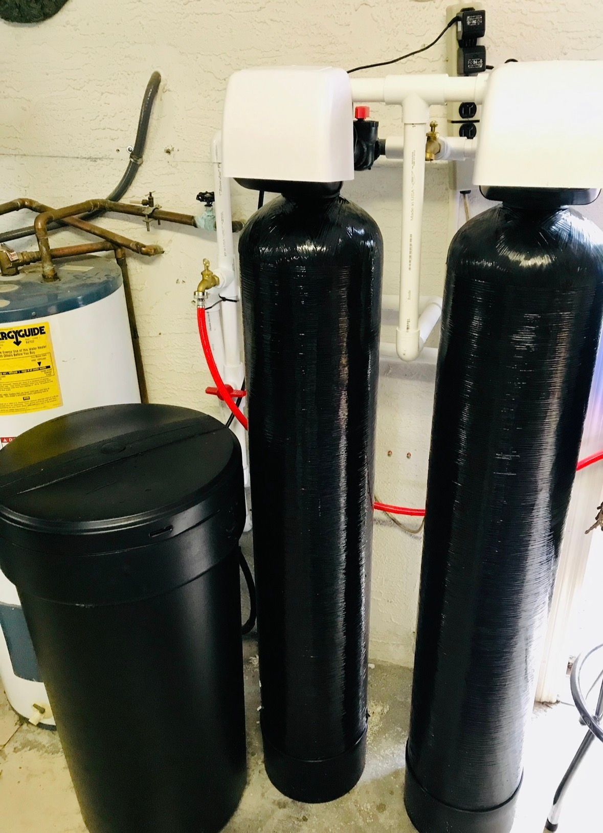 Two black water softener tanks beside a black brine tank in a utility room