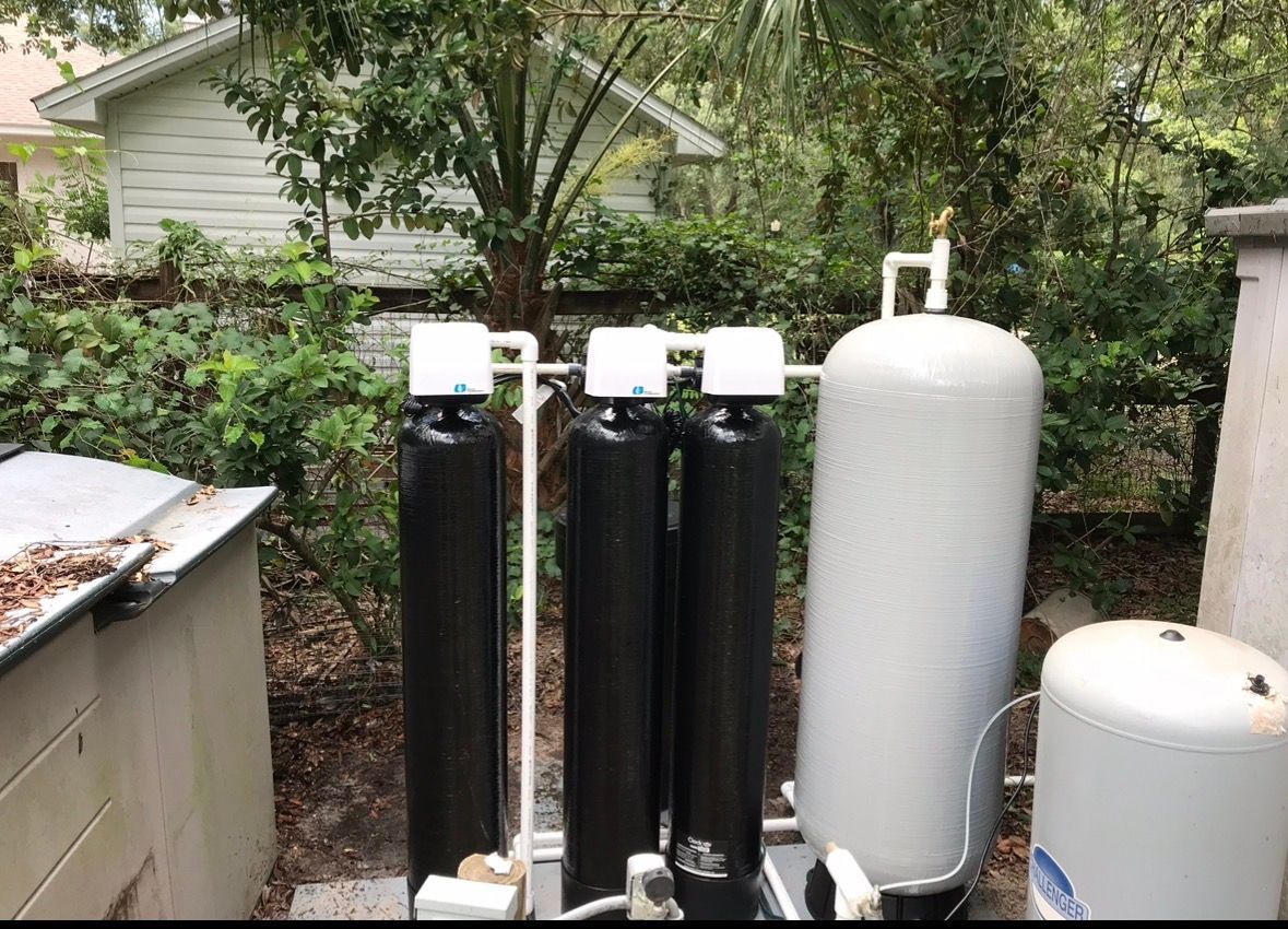 Outdoor water softener tanks and filtration equipment beside a house in a backyard