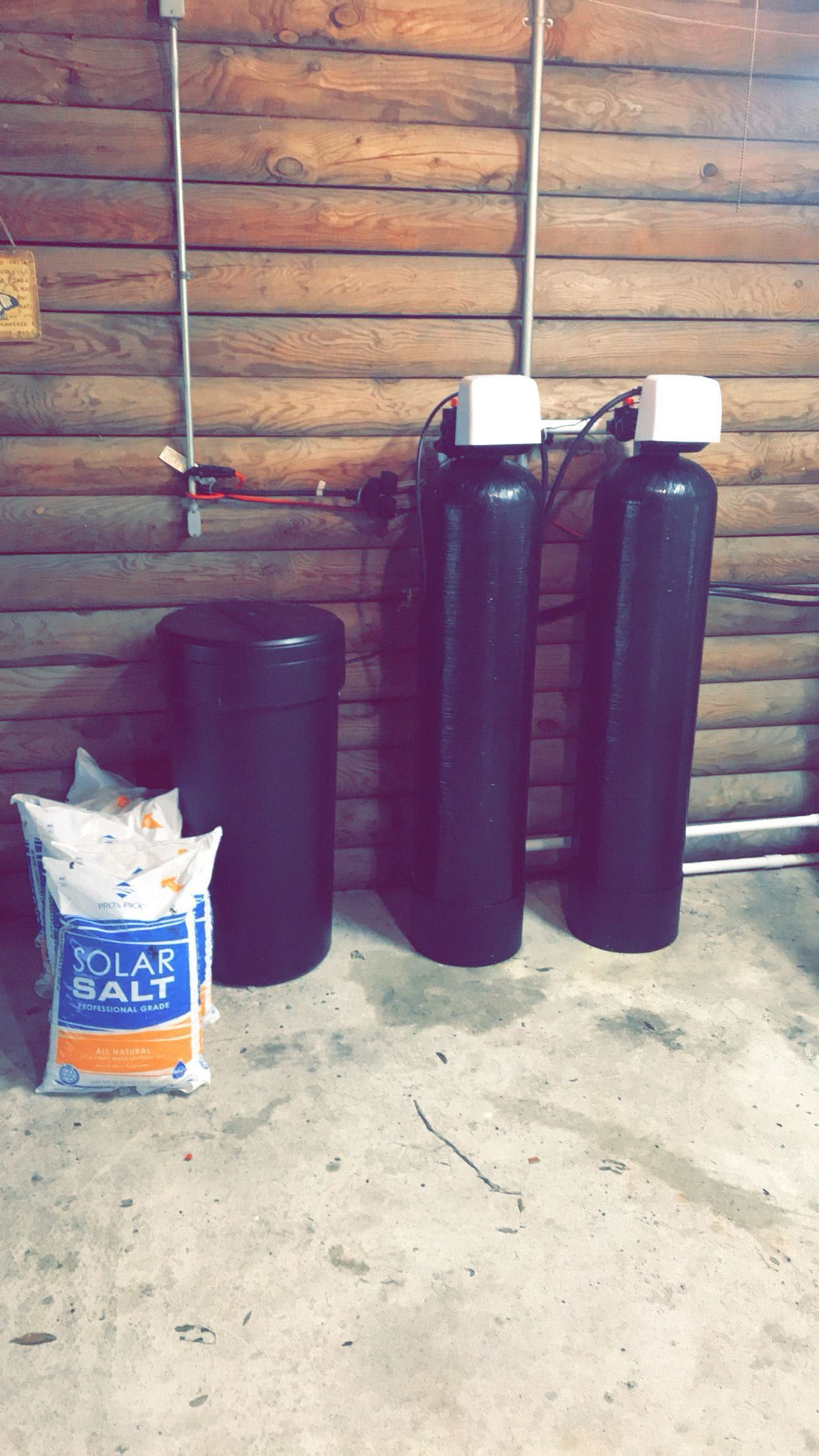 Two black propane tanks and a bag on a concrete floor against a wooden wall.